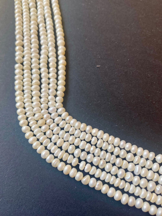 A beautiful strand of smooth white rondelle freshwater pearls, measuring 3.5-4.0mm, resting on a dark black surface.