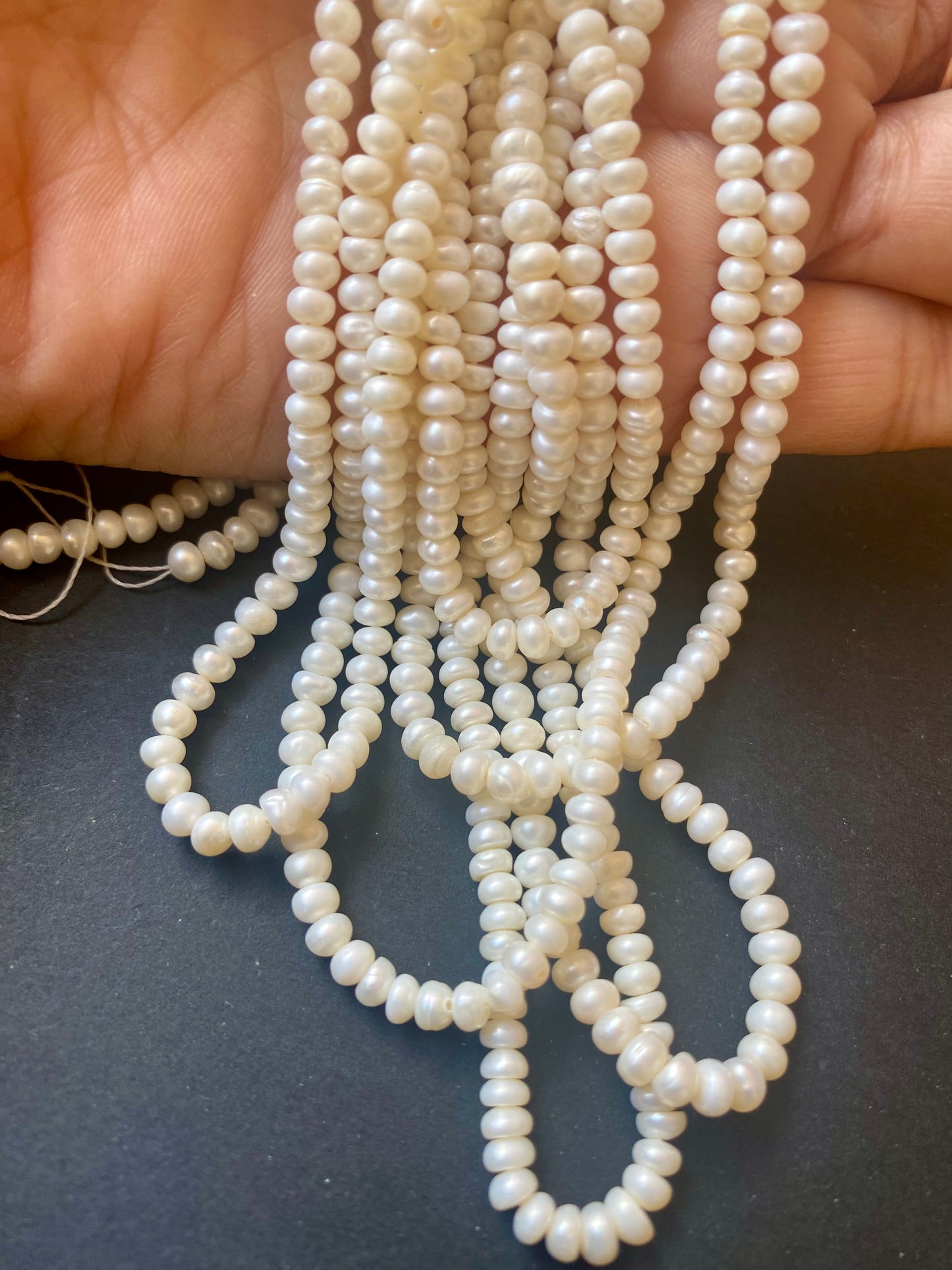A hand gracefully holds a cluster of smooth, white freshwater pearls, each bead measuring 3.5-4.0mm in size.