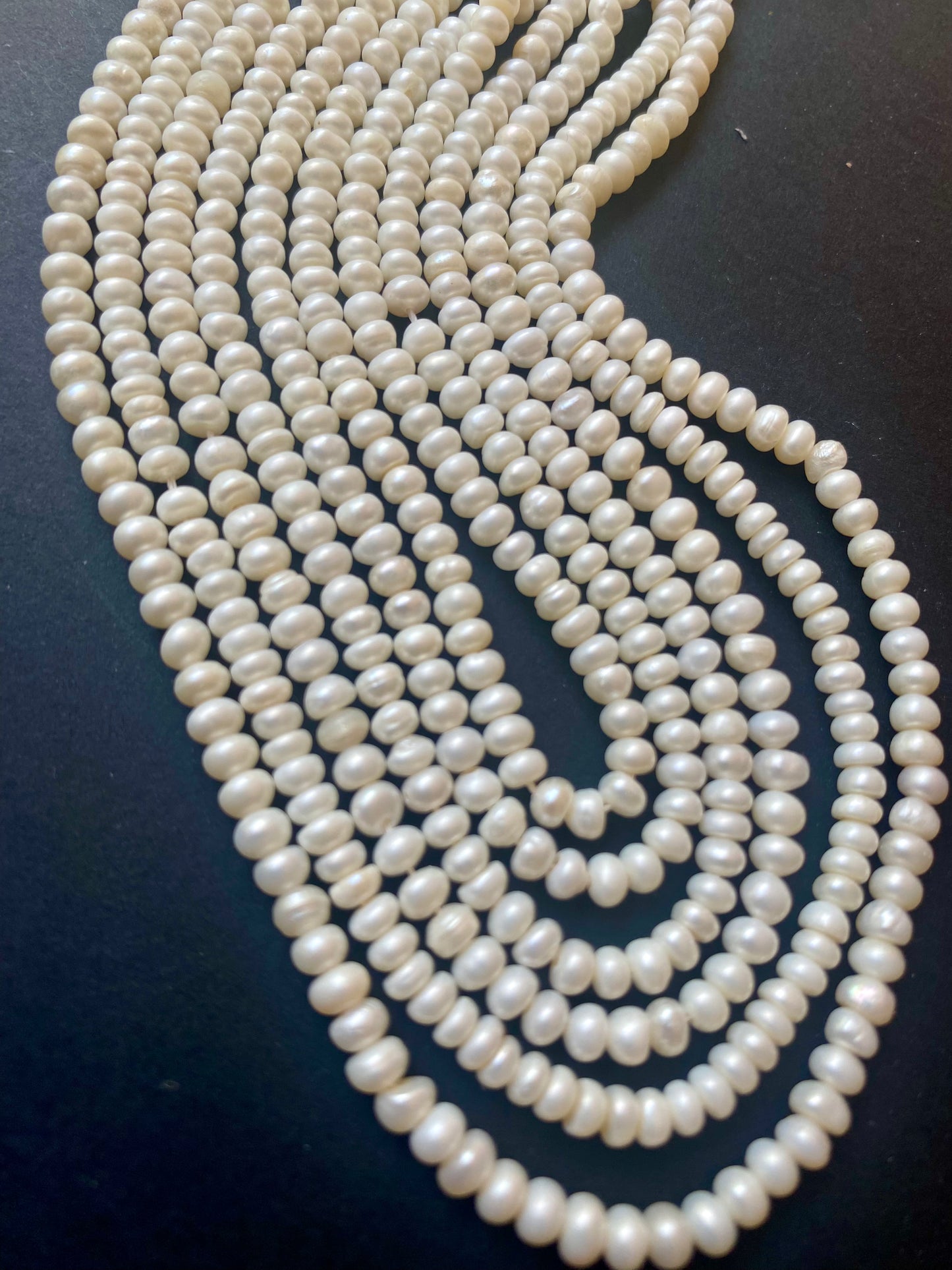A multiple strands of smooth white freshwater pearls, 3.5-4.0mm, elegantly displayed on a sleek black surface.