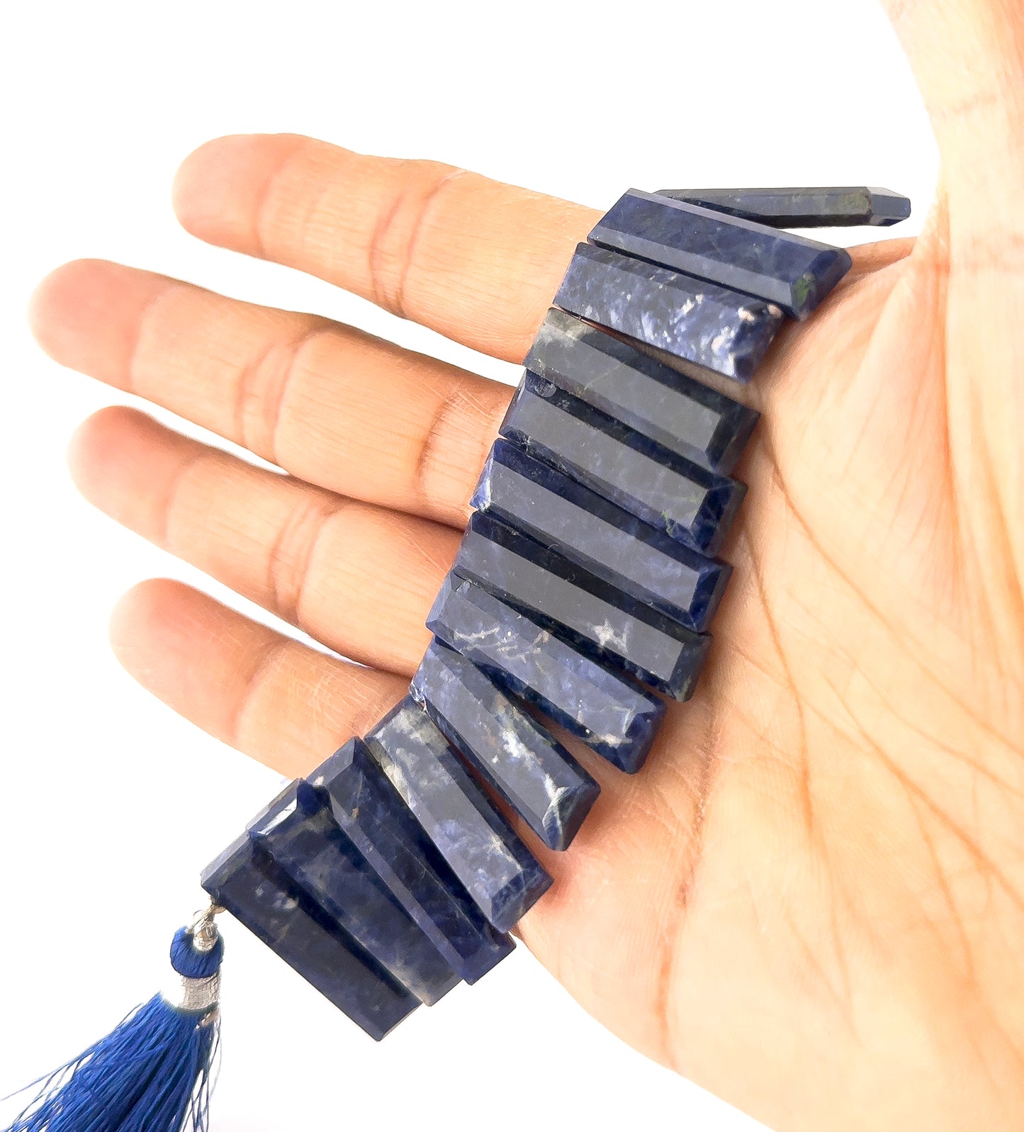 A person holds Sodalite faceted rectangle beads, showing their geometric design and intense blue colour.
