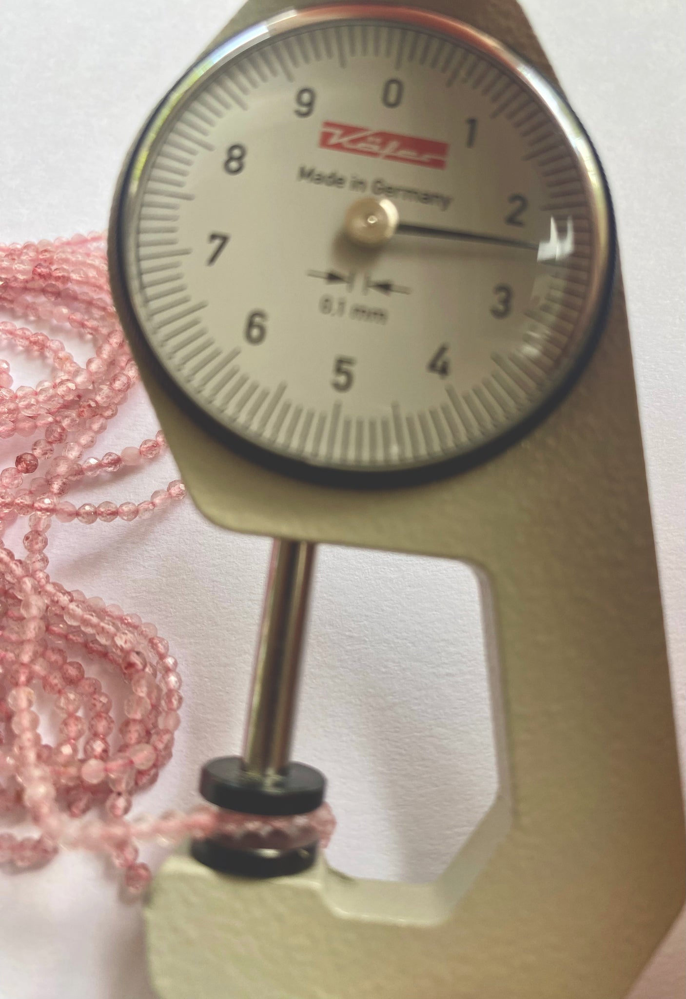 A dial gauge measures the Strawberry Quartz faceted rondelle gemstone beads, ensuring precise 2.3mm or 2.4-2.5mm sizing.