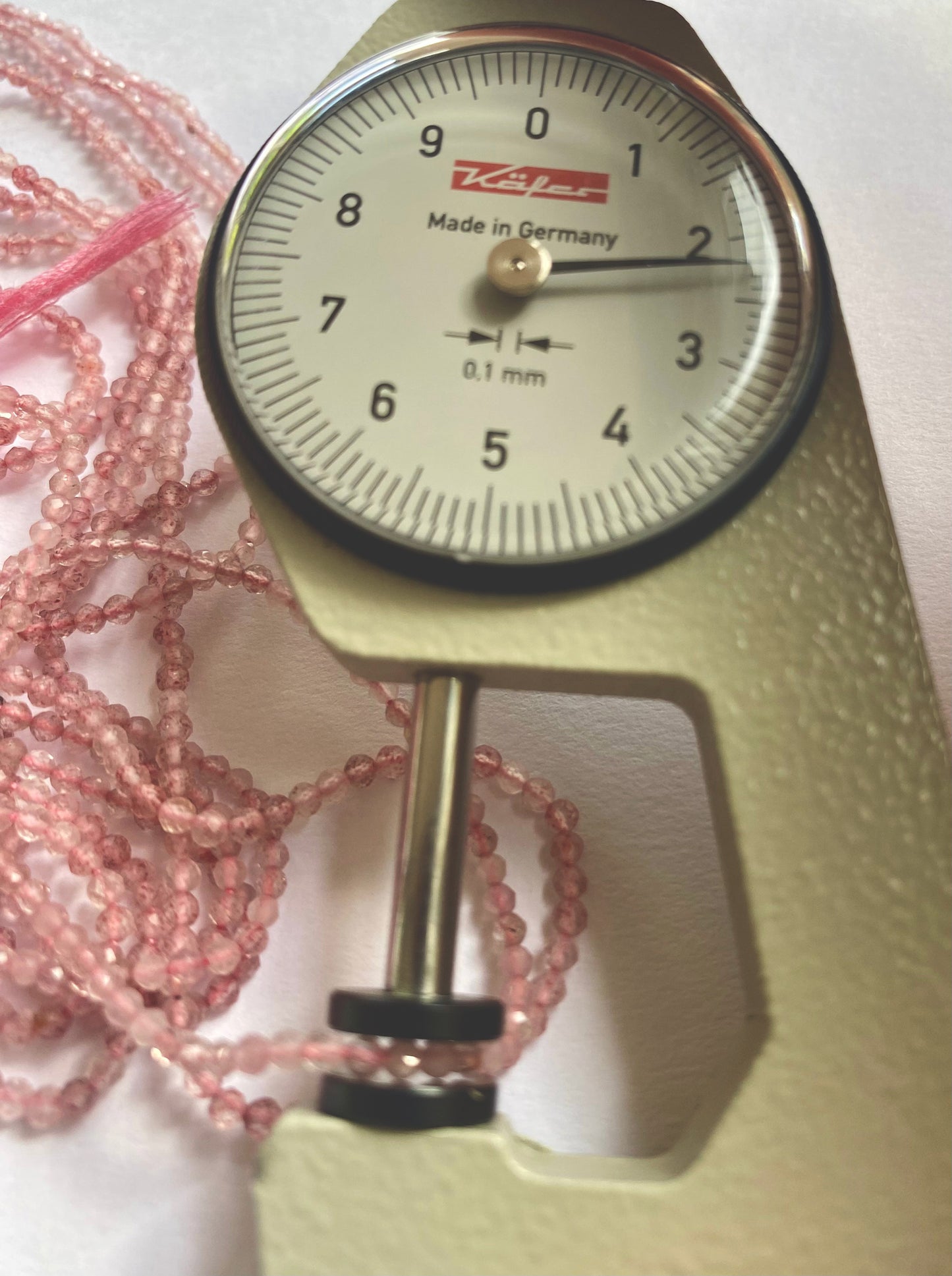 A dial gauge measures the Strawberry Quartz faceted rondelle gemstone beads, ensuring precise 2.3mm or 2.4-2.5mm sizing.