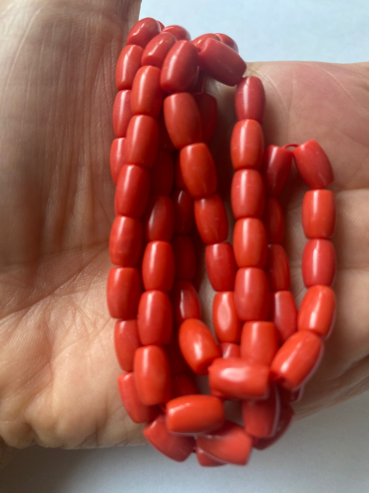 A hand delicately holds a strand of Taiwan Coral Gemstone Beads, showcasing their lustre and elegance.