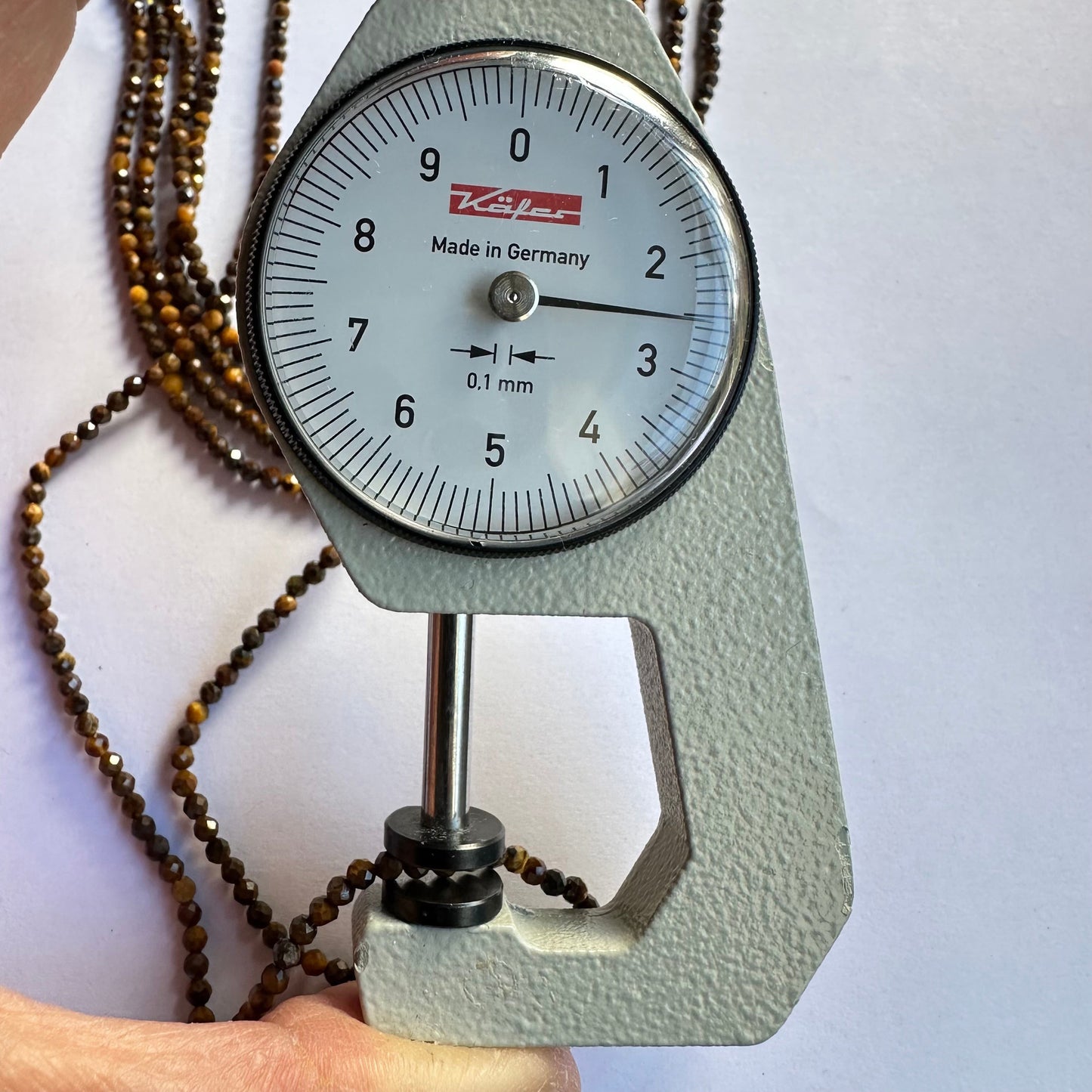 A dial gauge measures the Tiger Eye micro-faceted rondelle 2.5mm gemstone, confirming size precision.