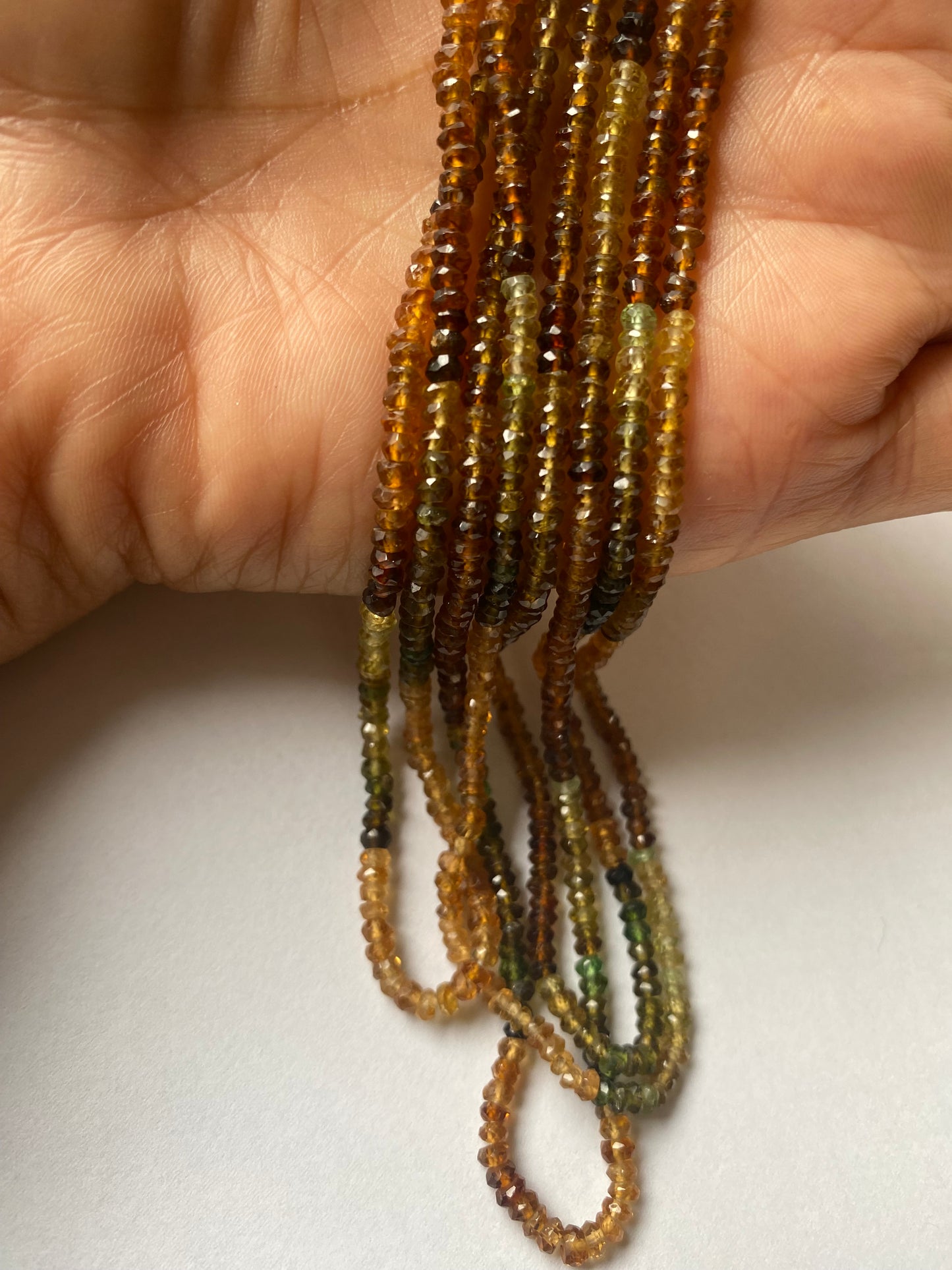 Close-up of a person’s hand showcasing a colourful assortment of 3-3.5mm tourmaline beads.