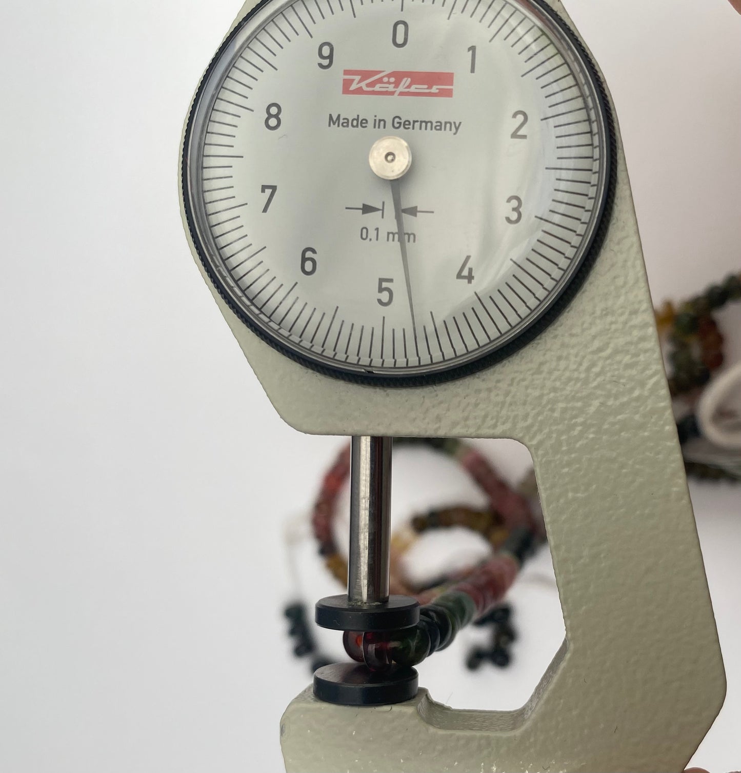Close-up of a measuring dial gauge alongside a vibrant collection of 4.5-5mm faceted rondelle tourmaline beads.
