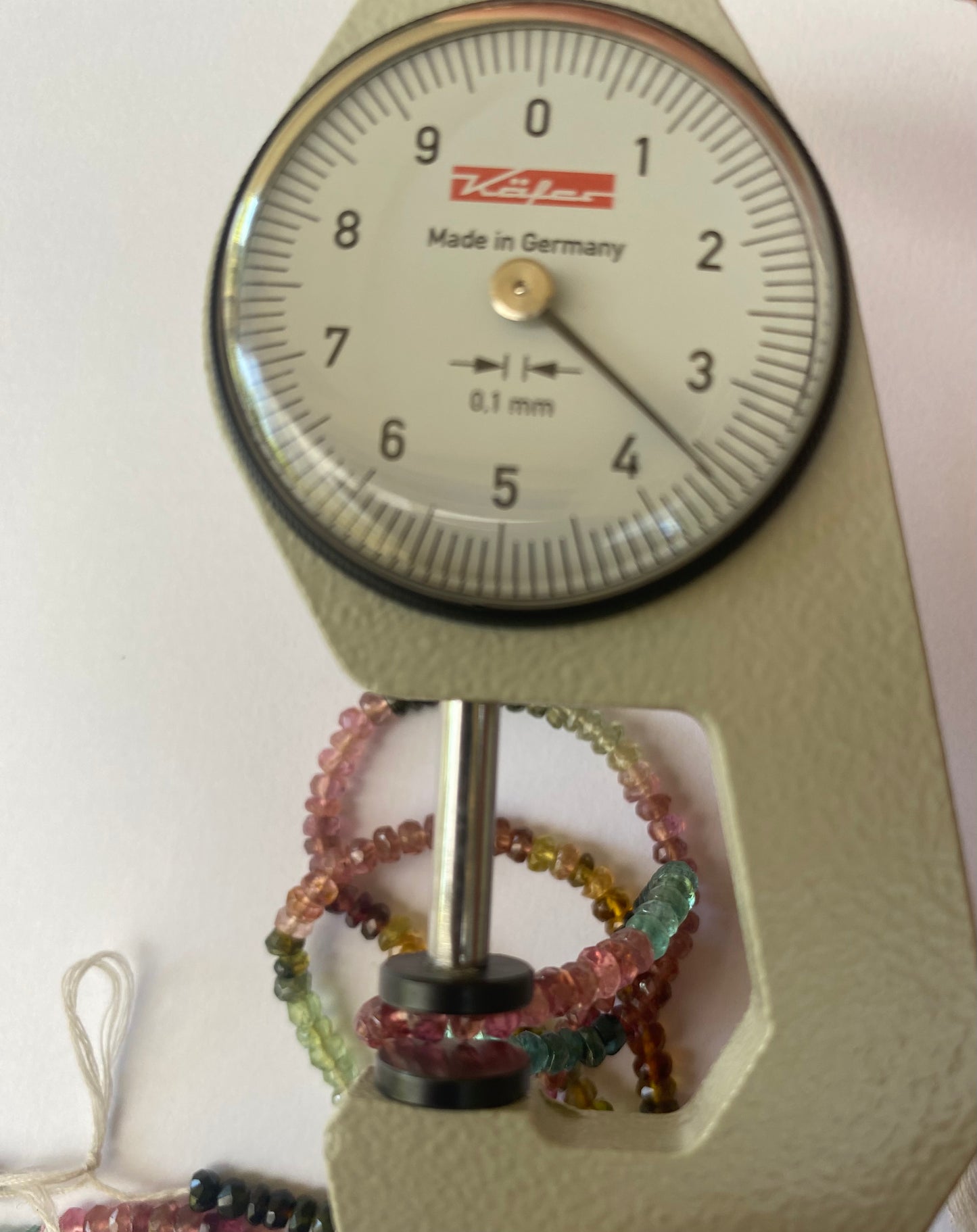 A person uses a measuring tape and wears a watch, highlighting a semi-precious tourmaline of 3.5-3.9mm in size