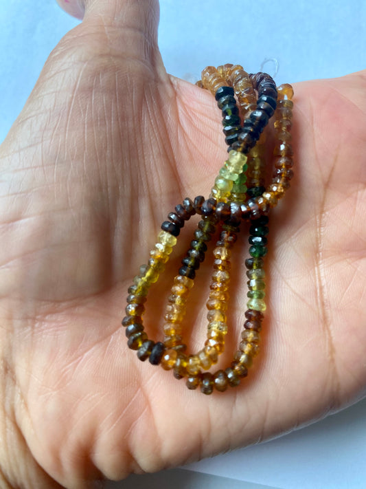 A hand delicately holds a strand of 4mm tourmaline strand, showcasing their lustre and elegance.