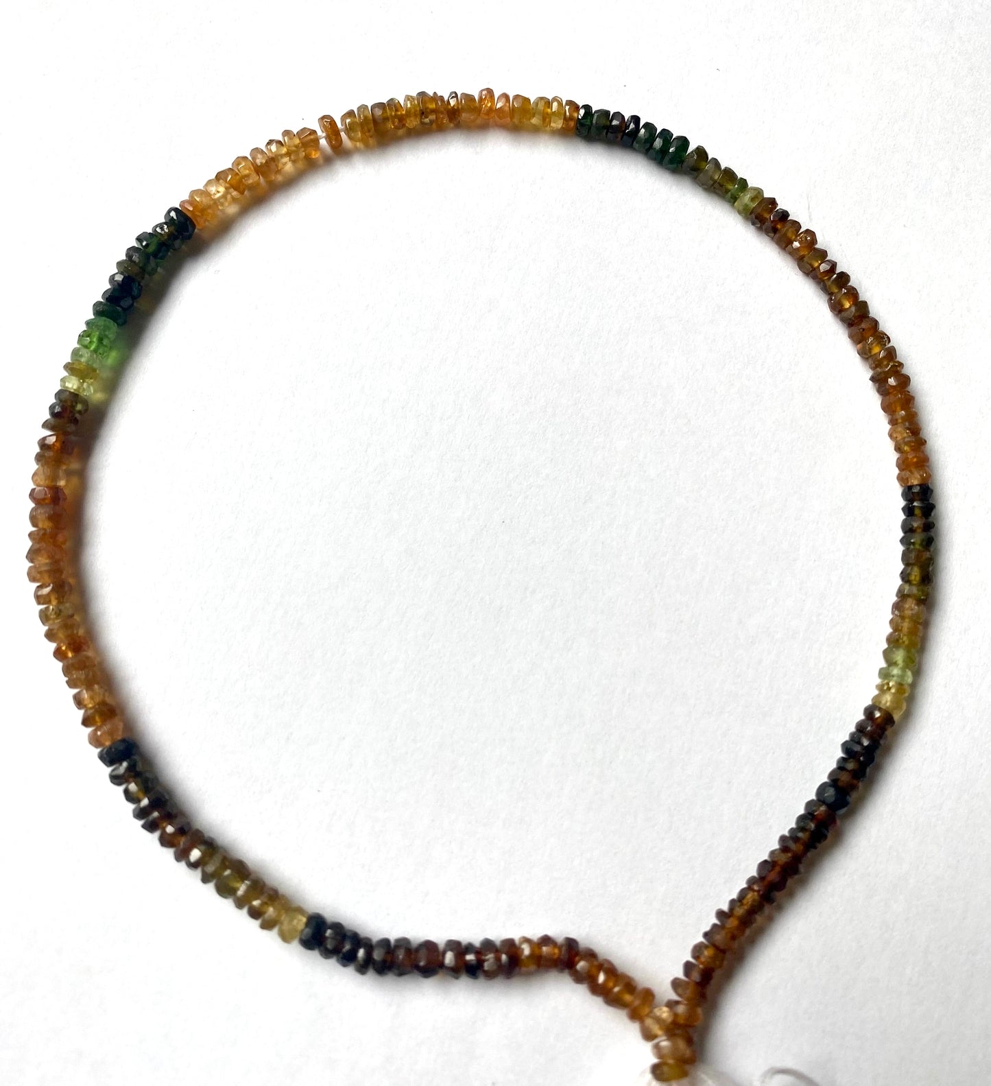 A delicate strand of 4mm Tourmaline elegantly displayed on a smooth white surface.