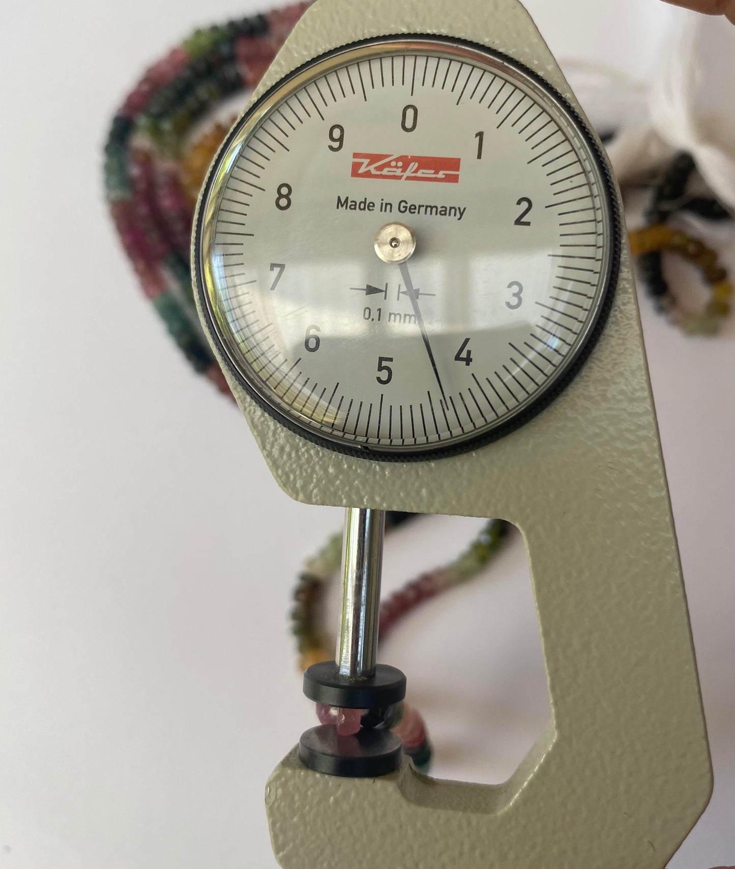 Close-up of a gauge measuring a string of faceted tourmaline rondelle beads, measuring 4.4-4.8mm.