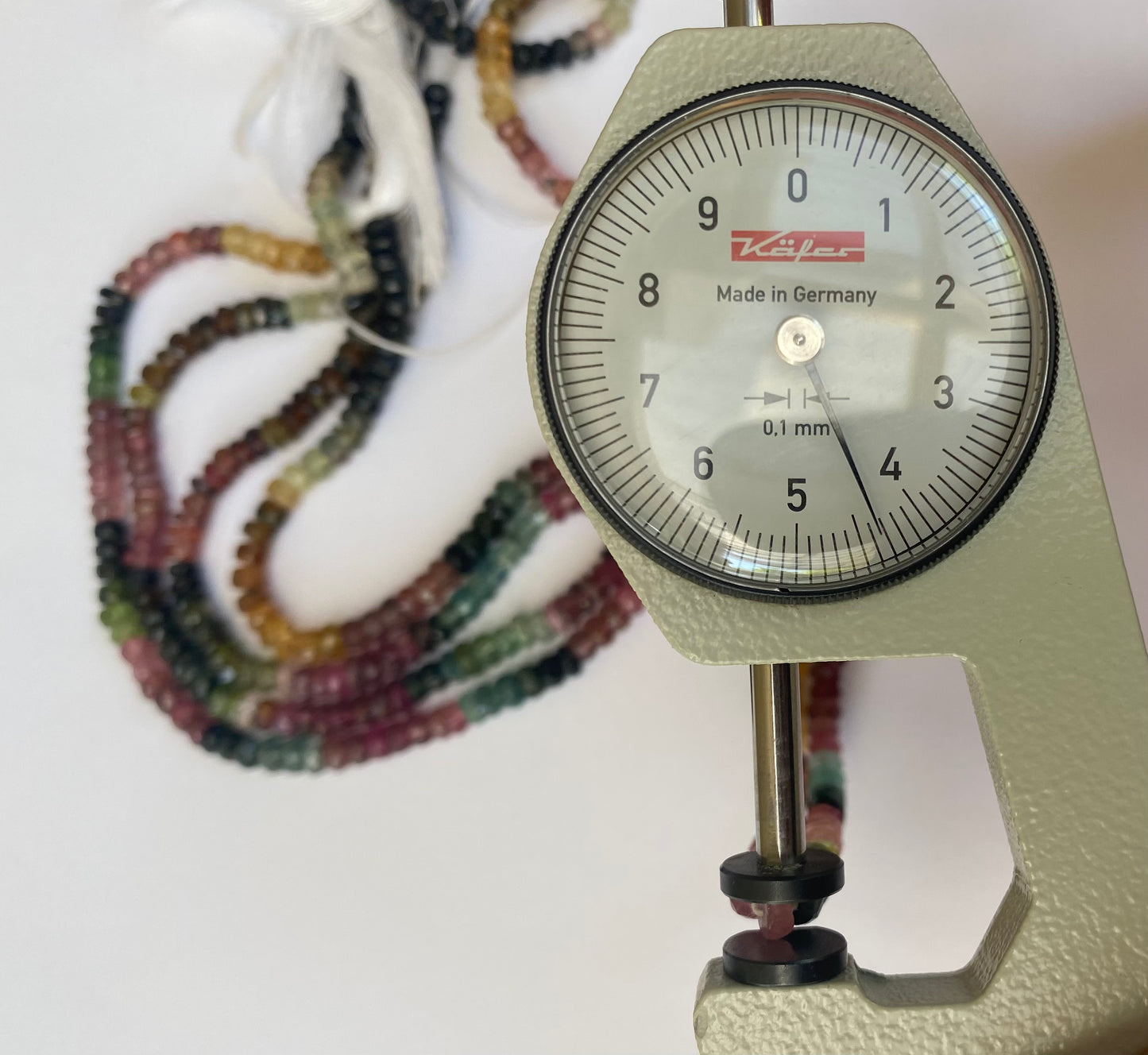 Detailed view of a dial gauge tool with a string of 4.4-4.8mm faceted tourmaline rondelle beads.