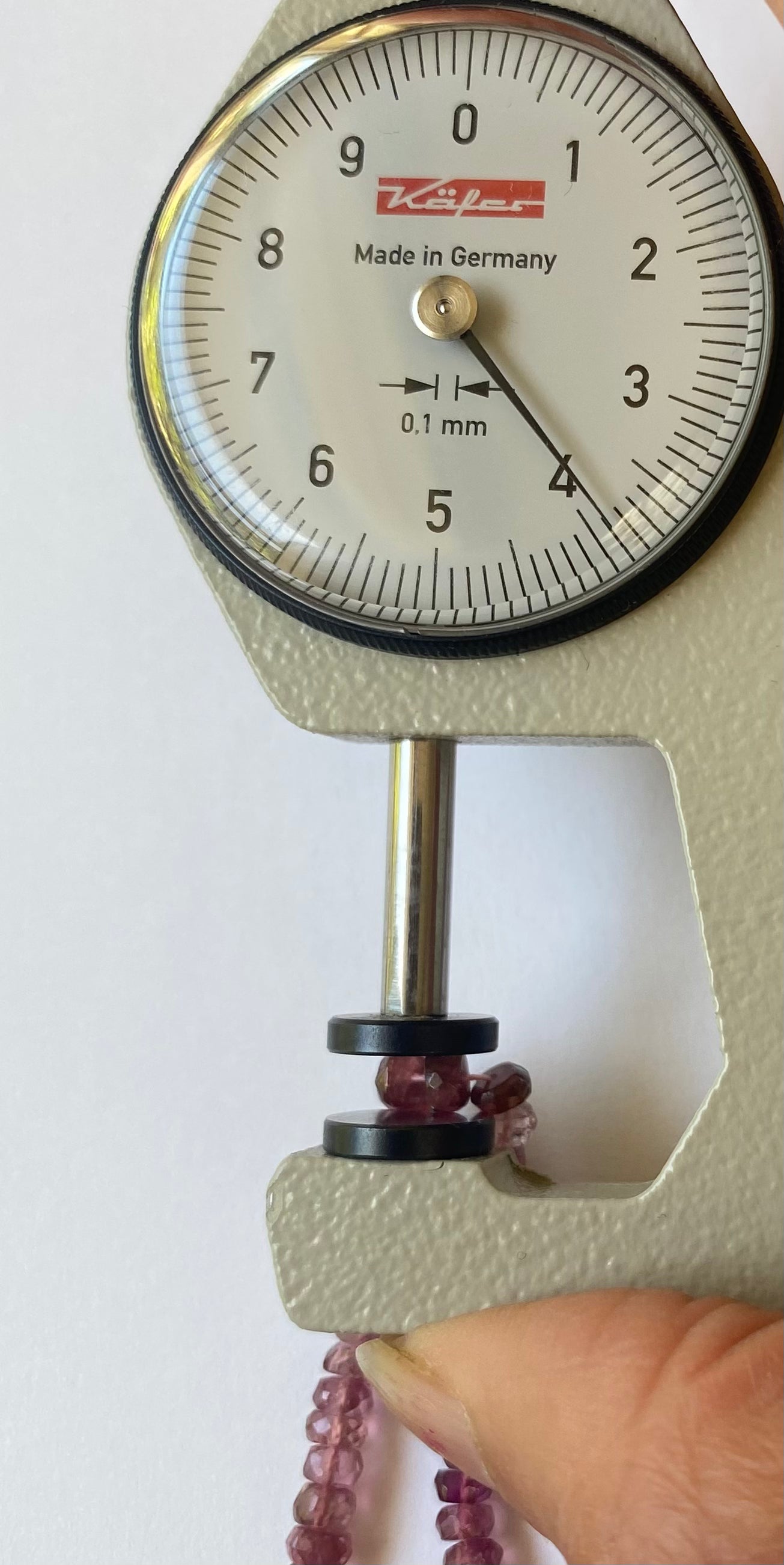 A hand grips a small gauge featuring a red faceted tourmaline rondelle bead, sized between 3.8 and 4.0mm.