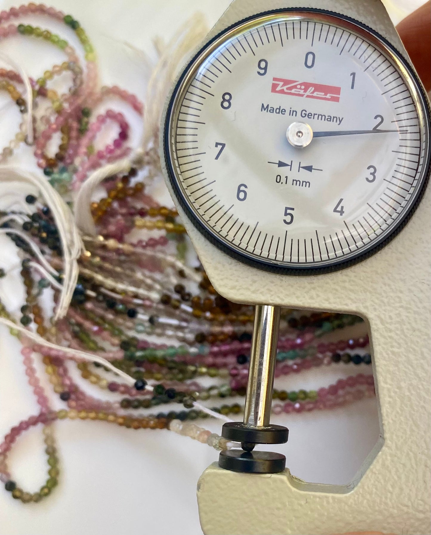 A person measuring colourful 2.2mm micro-faceted tourmaline beads with a scale measure in hand.
