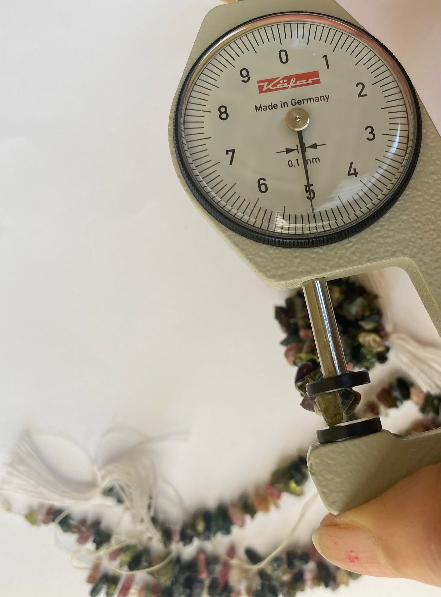 A person measuring tourmaline rough beads, 3-6mm, with a measuring tape while holding a piece of jewellery.