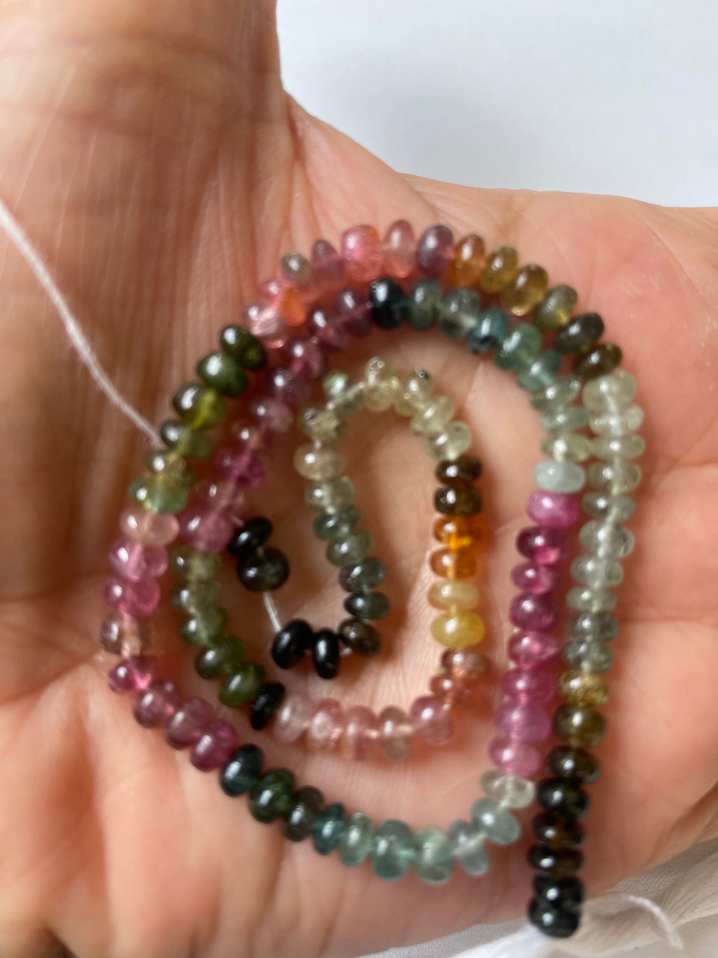 A person holding a vibrant bunch of 5mm tourmaline beads in various colours.
