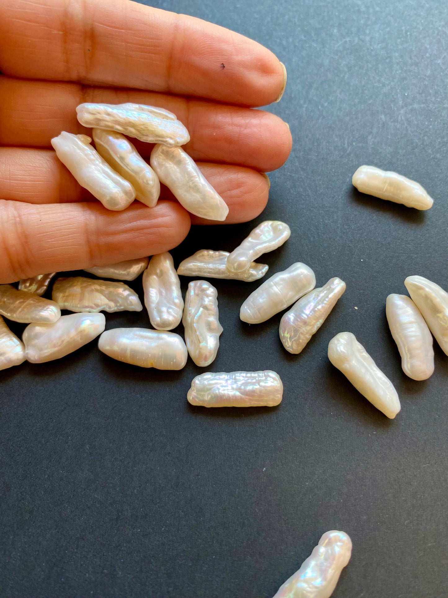 A person holding a cluster of undrilled Baroque pearls, showcasing their unique shapes and lustrous white sheen.