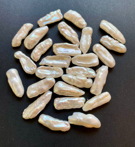 Undrilled Baroque white pearls displayed on a sleek black surface, showcasing their elegant, organic forms.