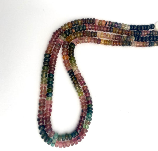 A row of vibrant watermelon tourmaline smooth rondelle beads in various colours on a white surface.
