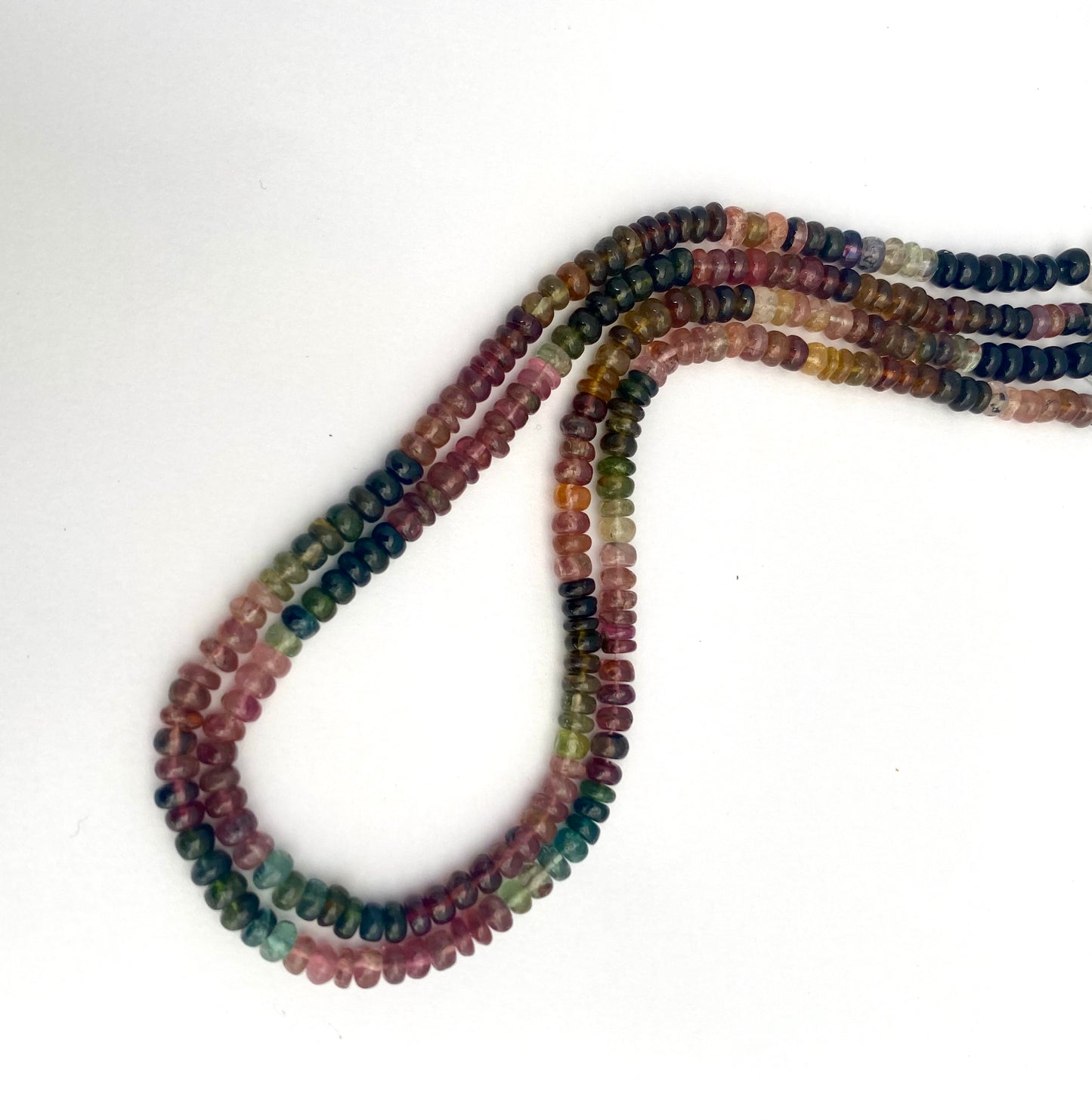 A colourful array of watermelon tourmaline smooth rondelle beads displayed on a white surface, showcasing their vibrant hues.