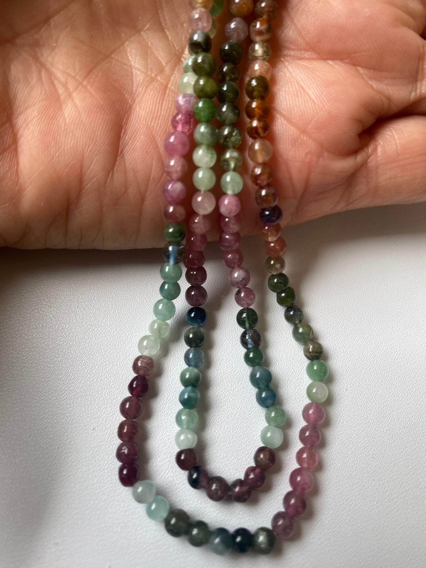 A person holding a vibrant bunch of 4.1 smooth round tourmaline beads in various colours.