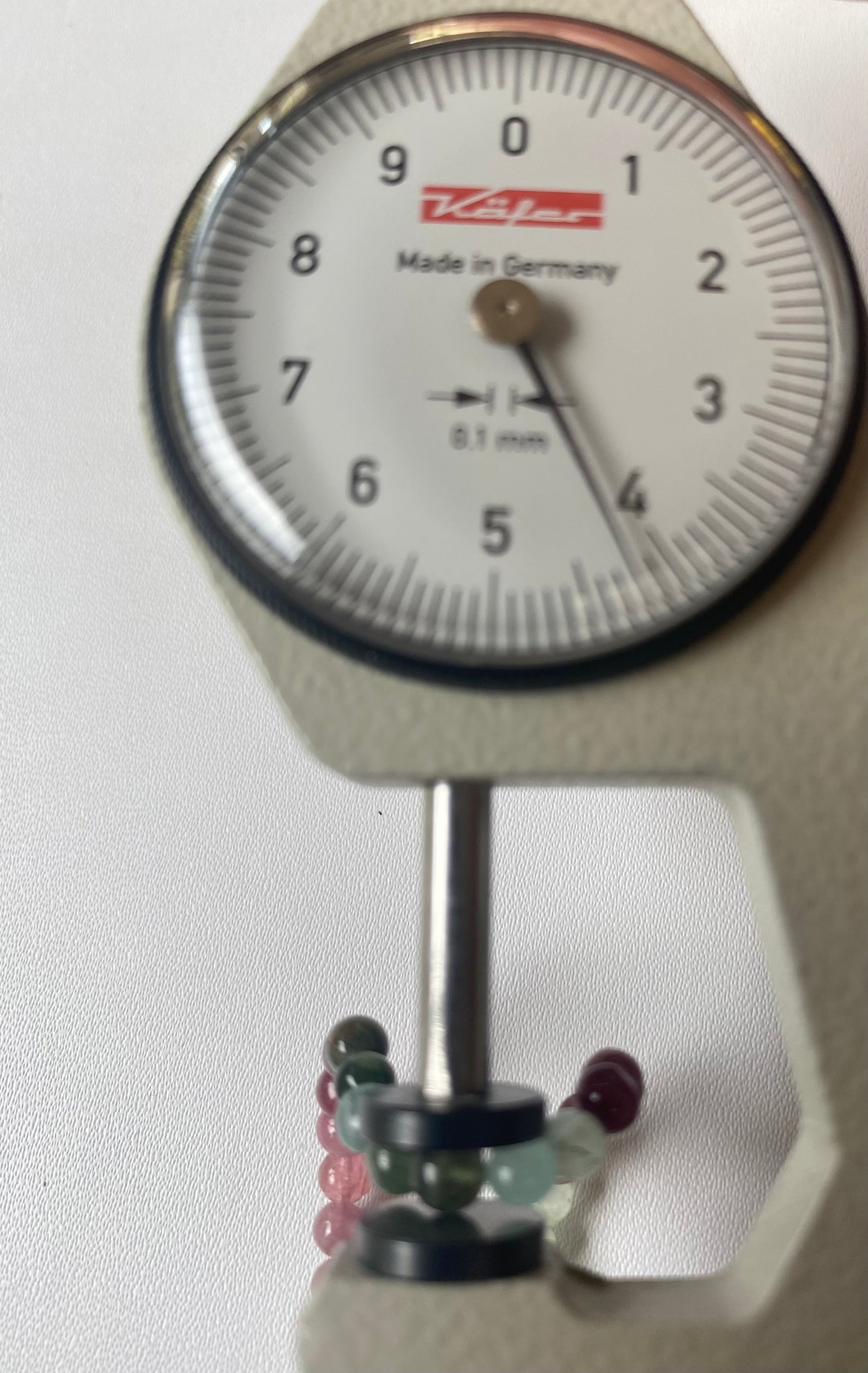 Close-up of a measuring dial gauge alongside a vibrant collection of 4.1mm of smooth round tourmaline beads.