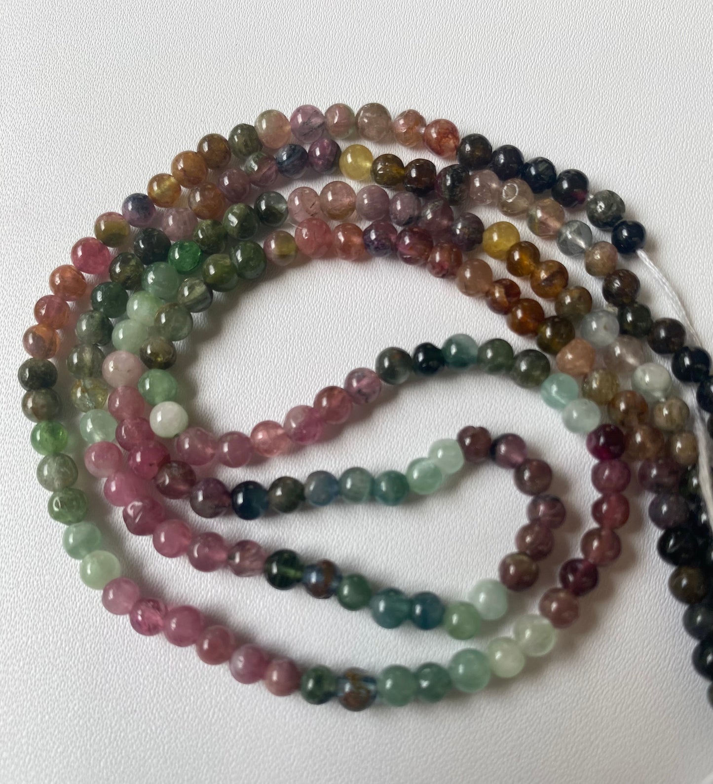 Multi-strands of micro-cut, 4.1mm multicoloured spherical tourmaline beads, showcasing vibrant hues and intricate design.