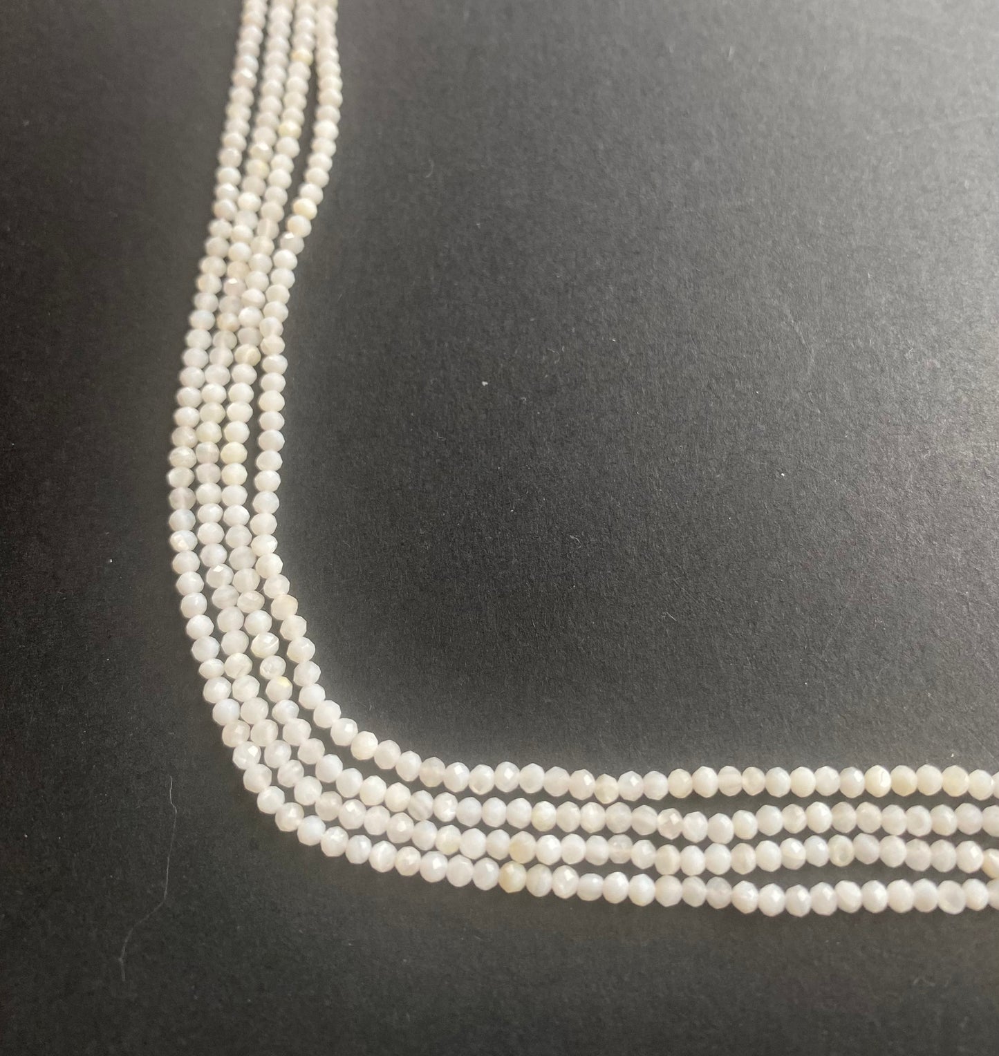A close-up of a multiple strands of white opal gemstone beads, faceted rondelles ranging from 2.25mm to 2.5mm, glistening in the light.