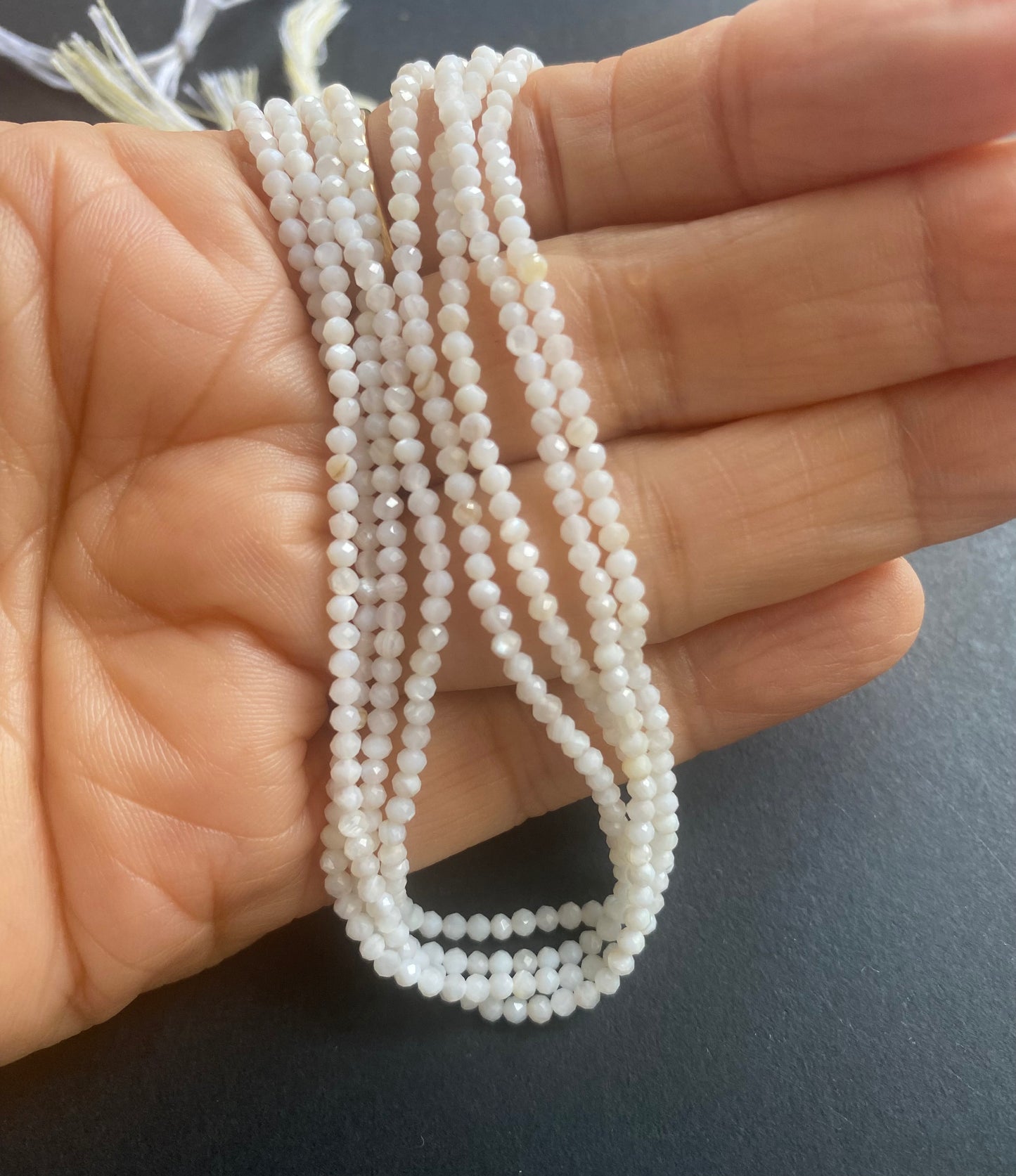 A person holding a smooth strand of Opal beads, measuring 2.25-2.5mm, showcasing their elegant white colour.
