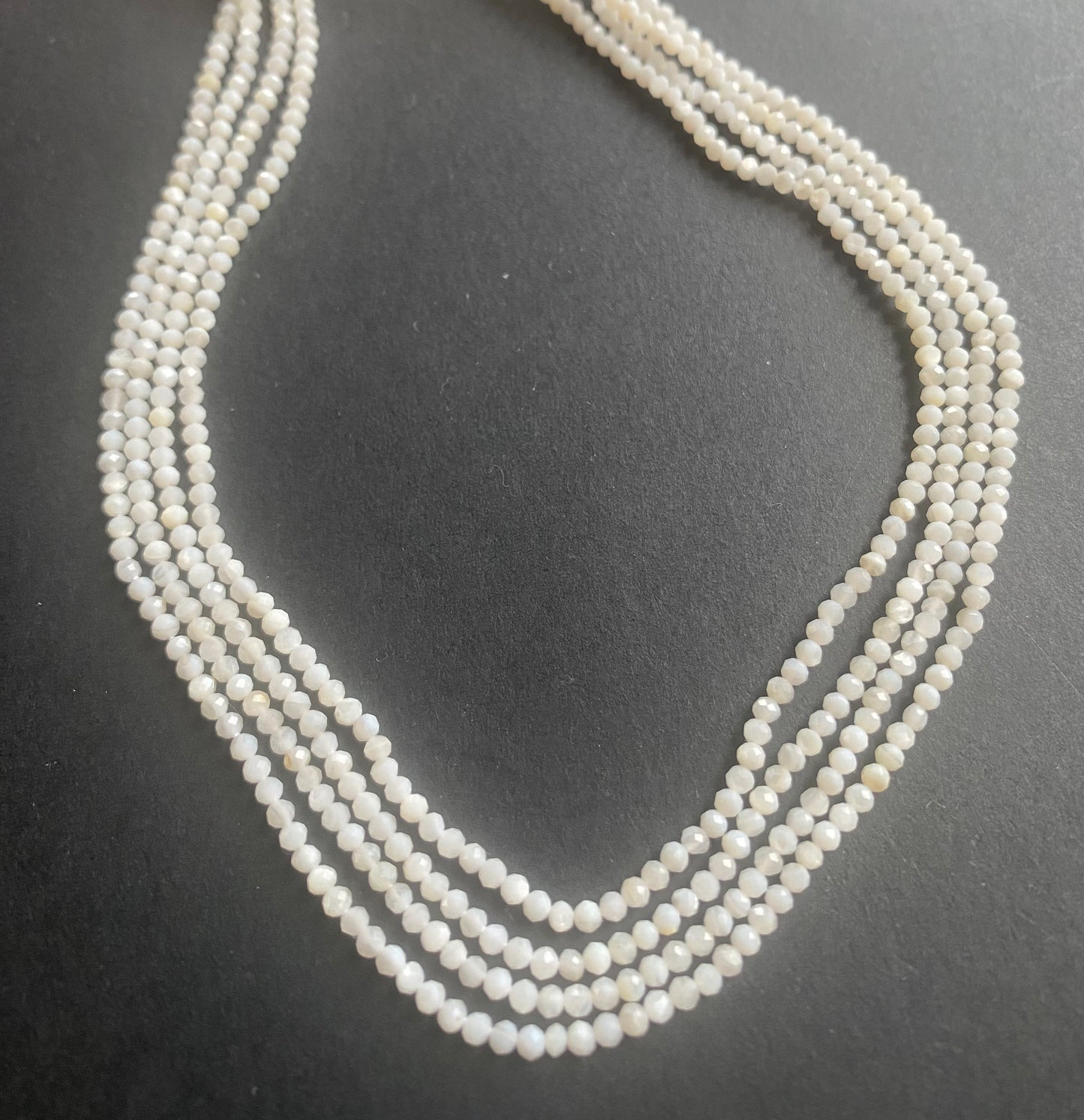 Close-up of a person grasping a strand of smooth white Opal beads, each 2.25-2.5mm in size, highlighting their beauty.