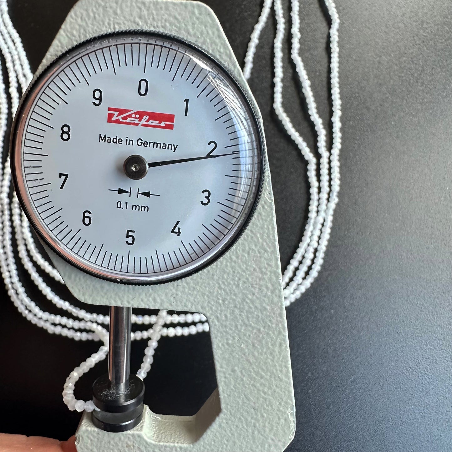 A dial gauge measures the White Rainbow Moonstone faceted rondelle 2.1mm gemstone, ensuring precision.