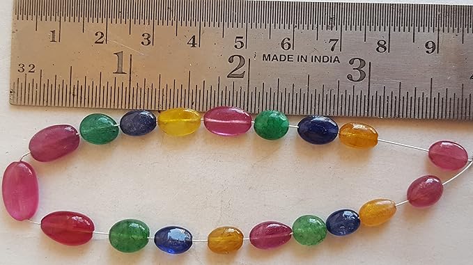 Close-up of a measuring ruler beside colourful multi-precious beads, including ruby, blue sapphire, yellow sapphire, and emerald.