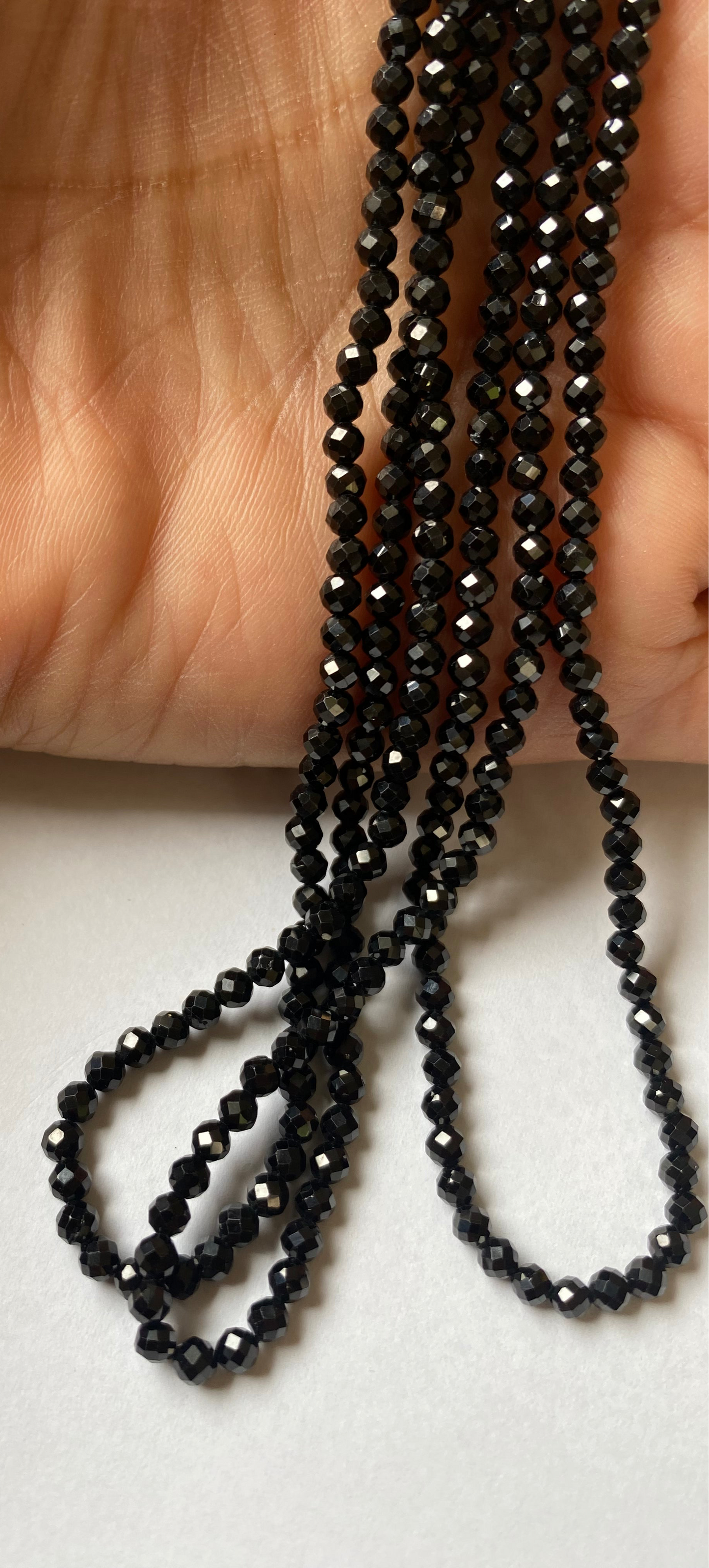Close-up of a person’s hand holding a delicate strand of 3.0mm black spinel micro-faceted rondelle beads.