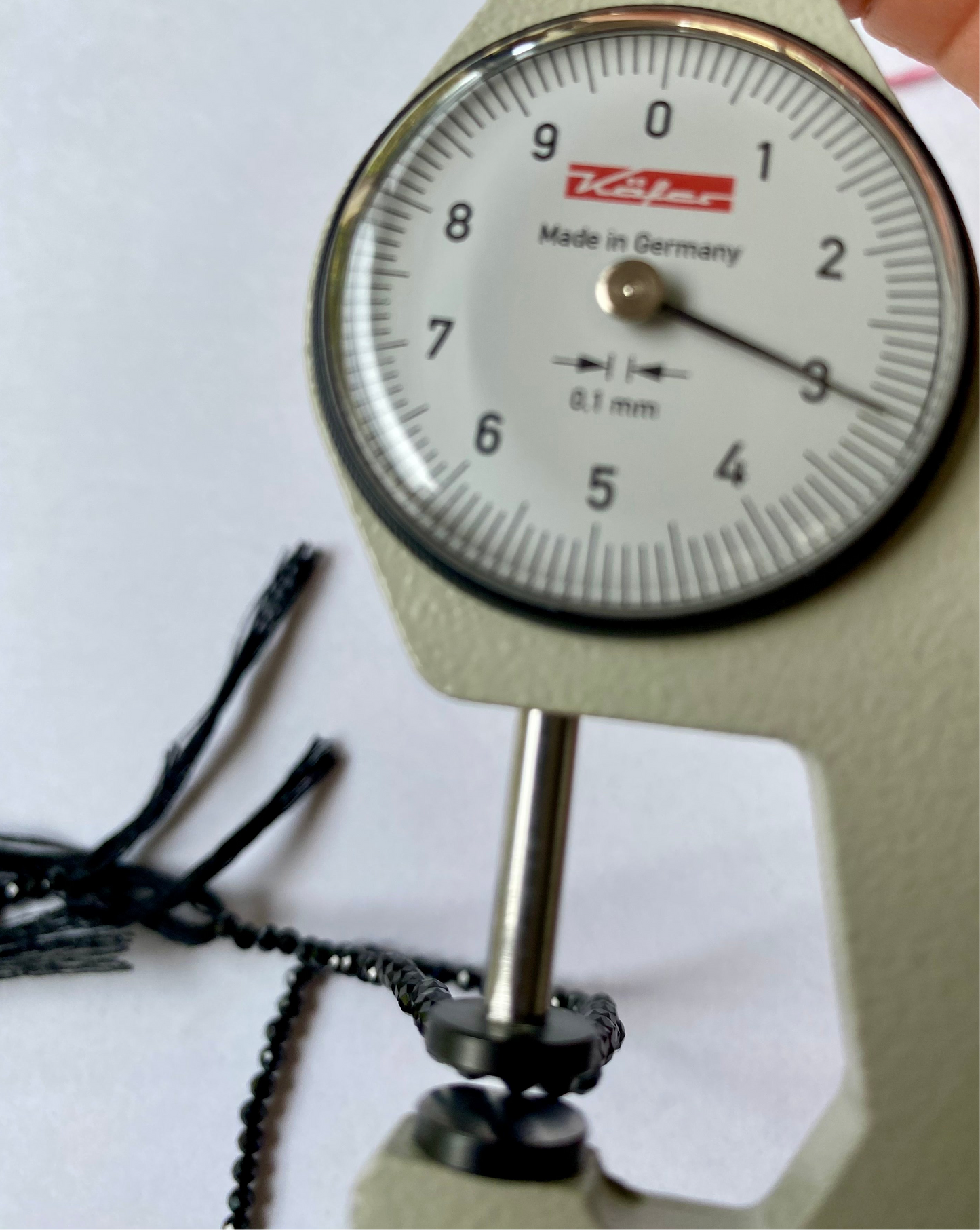 A dial gauge with a black bead on it next to a black gemstone strand featuring 3.0mm micro-faceted rondelle spinel beads.