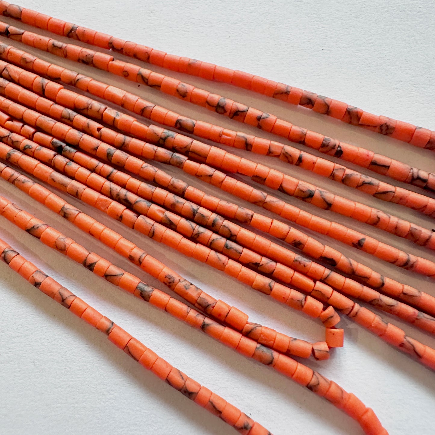 Afghan tube Heishi beads aligned for jewellery making, highlighting their subtle colour variation.