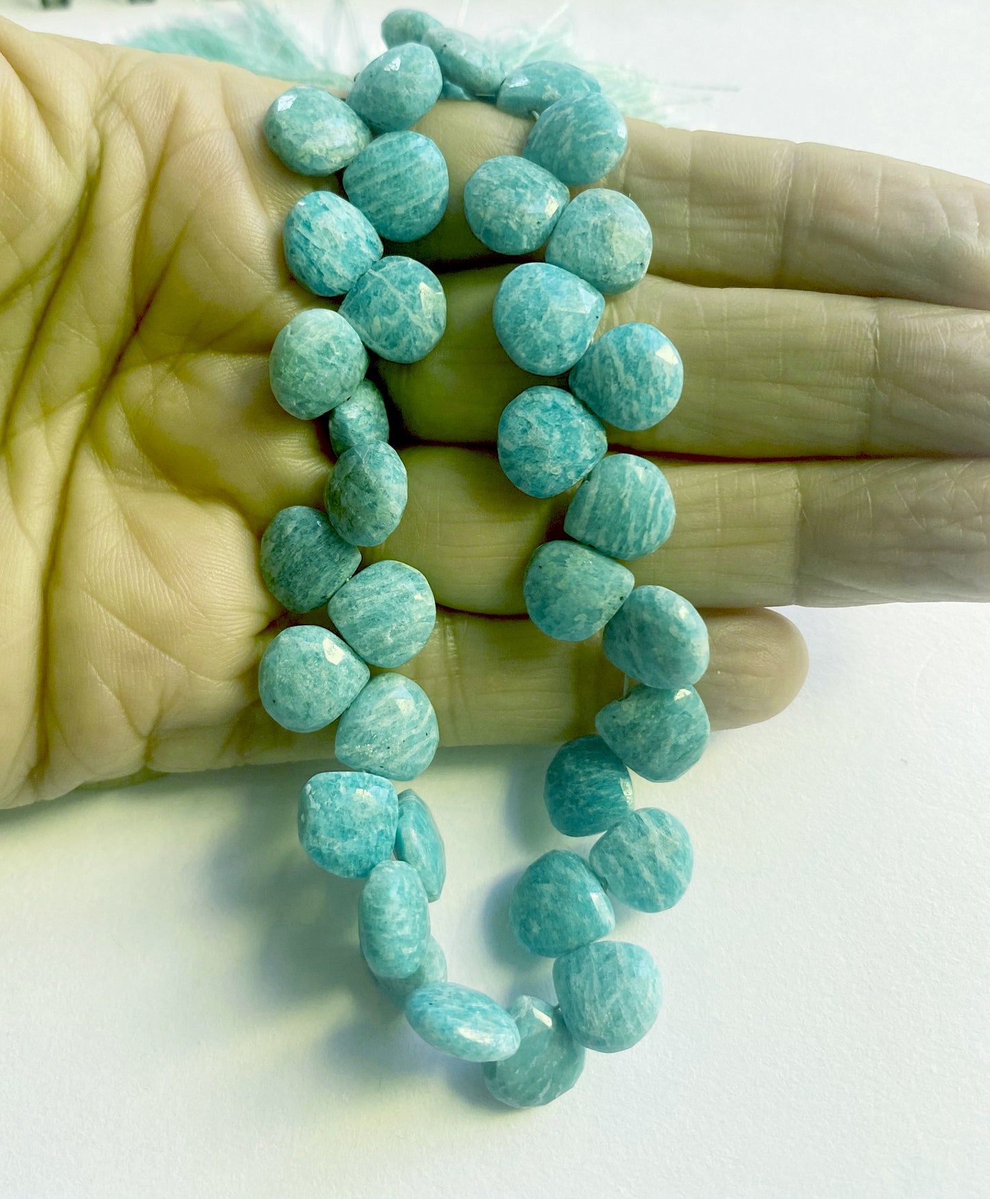 A person holds delicate strands of Amazonite beads, showcasing their faceted design.