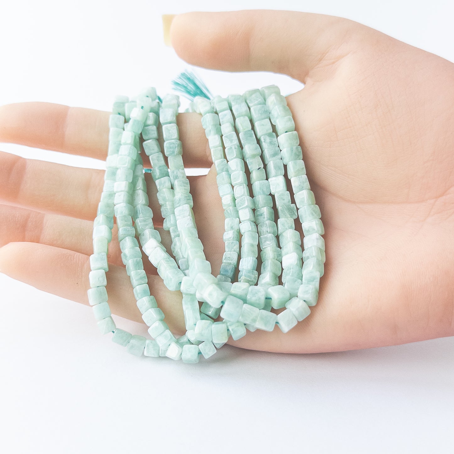 A person holds delicate strands of Amazonite smooth cube beads, showcasing their polished design.