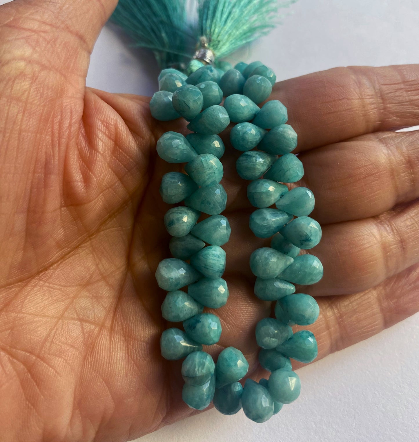 A person holds delicate strands of amazonite beads, showcasing their faceted design.