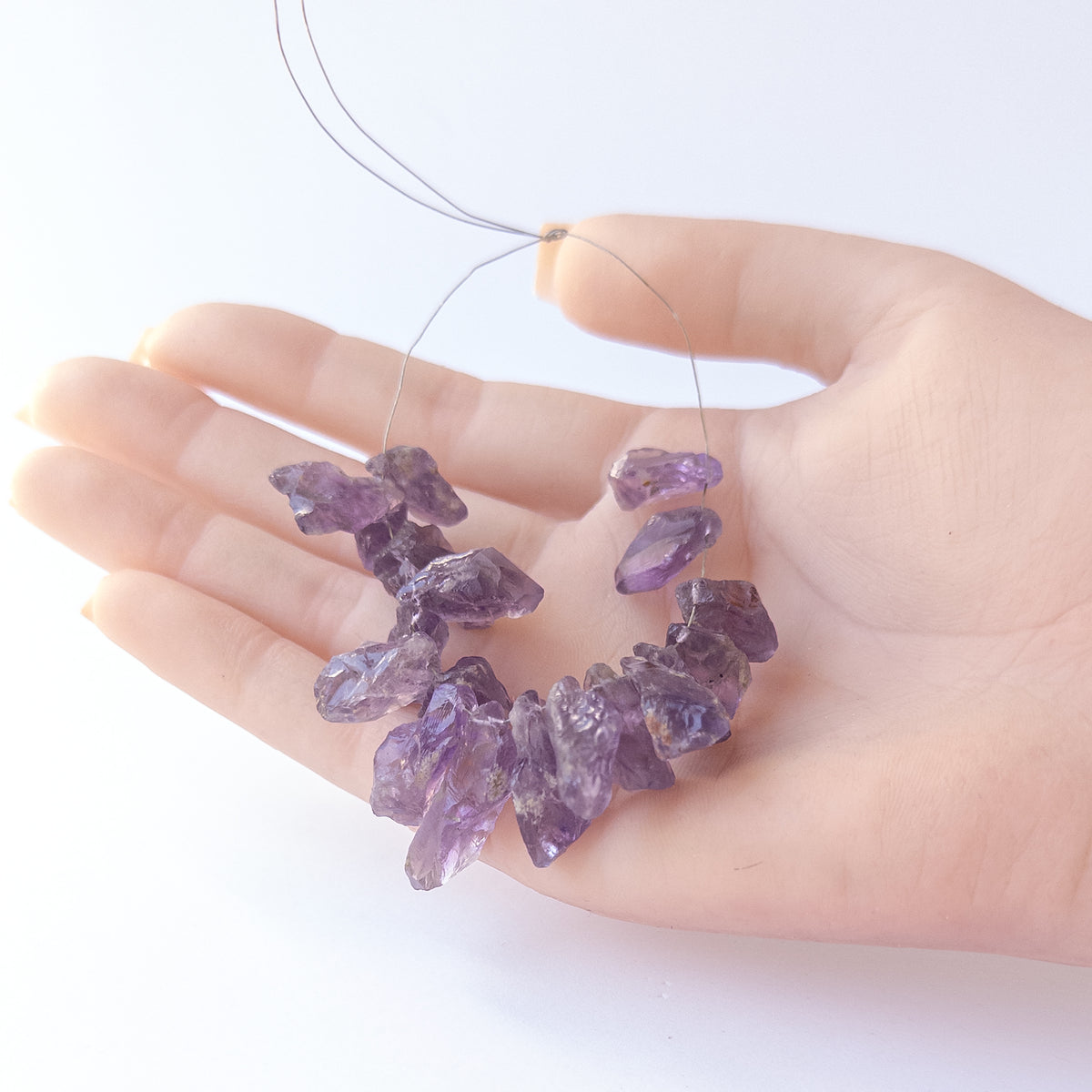A person holds delicate pieces of Amethyst rough beads, showcasing their drilled rough design.