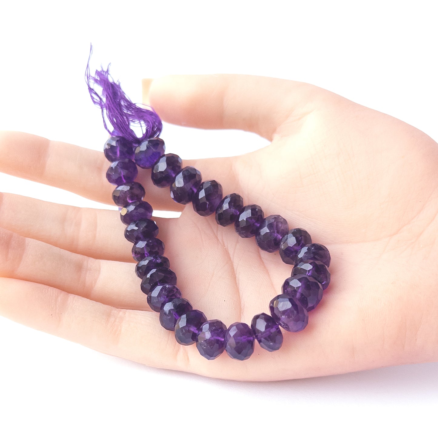 A person holds delicate strands of Amethyst beads, showcasing their faceted rondelle design.