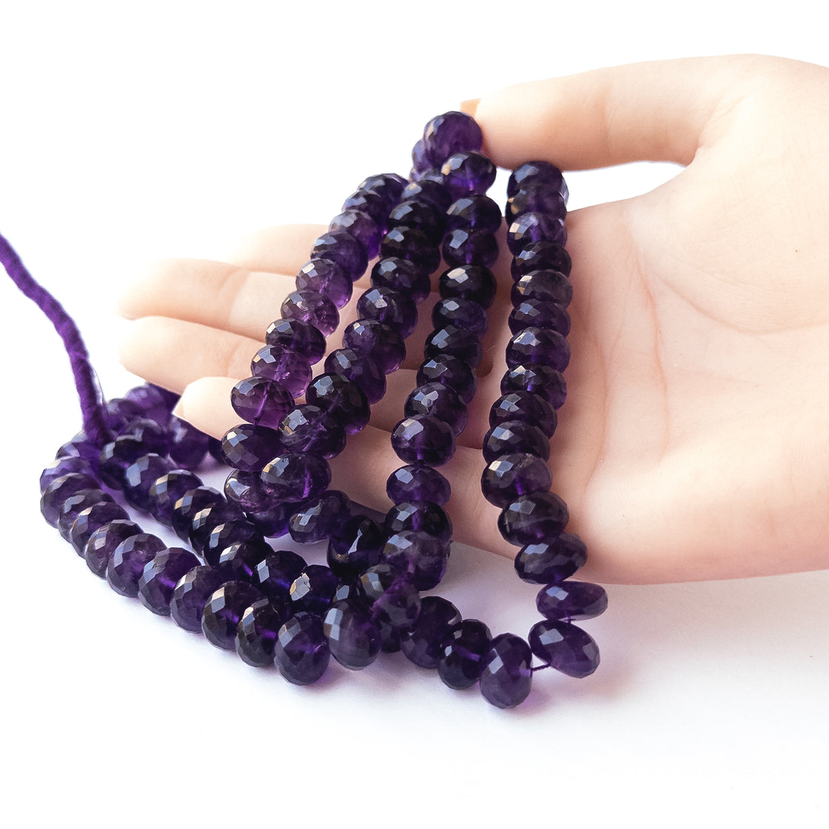 A person holds strands of Amethyst beads, showcasing their faceted rondelle design.