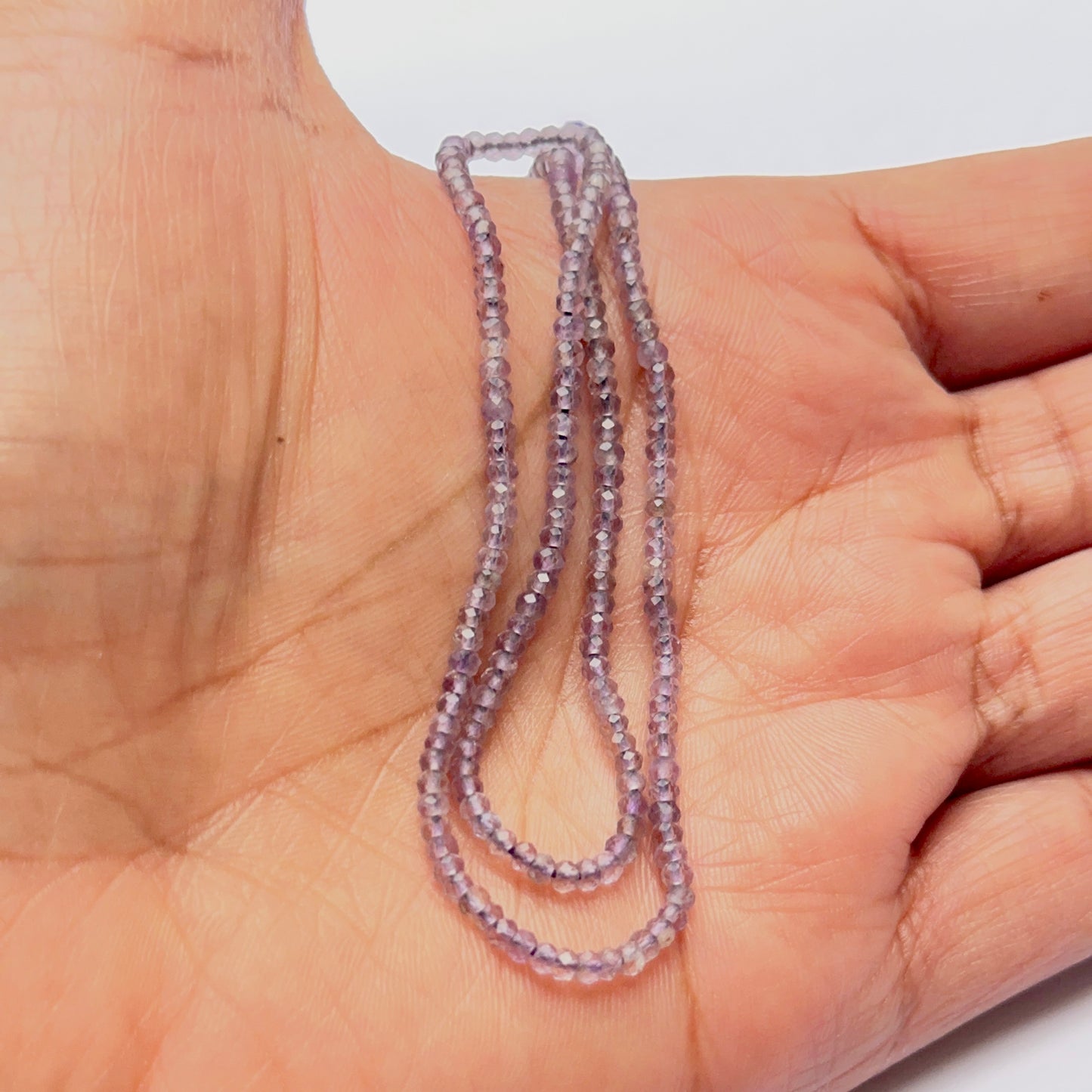 A person holds delicate strands of Amethyst beads, showcasing their smooth design.