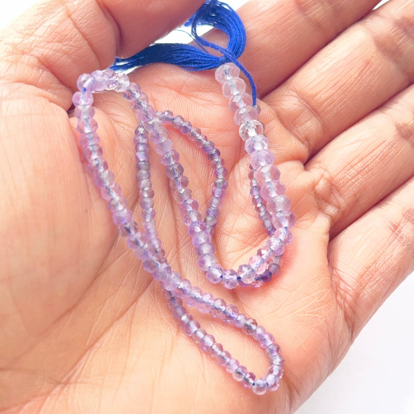 A person holds delicate strands of amethyst faceted beads, showcasing their smooth design.