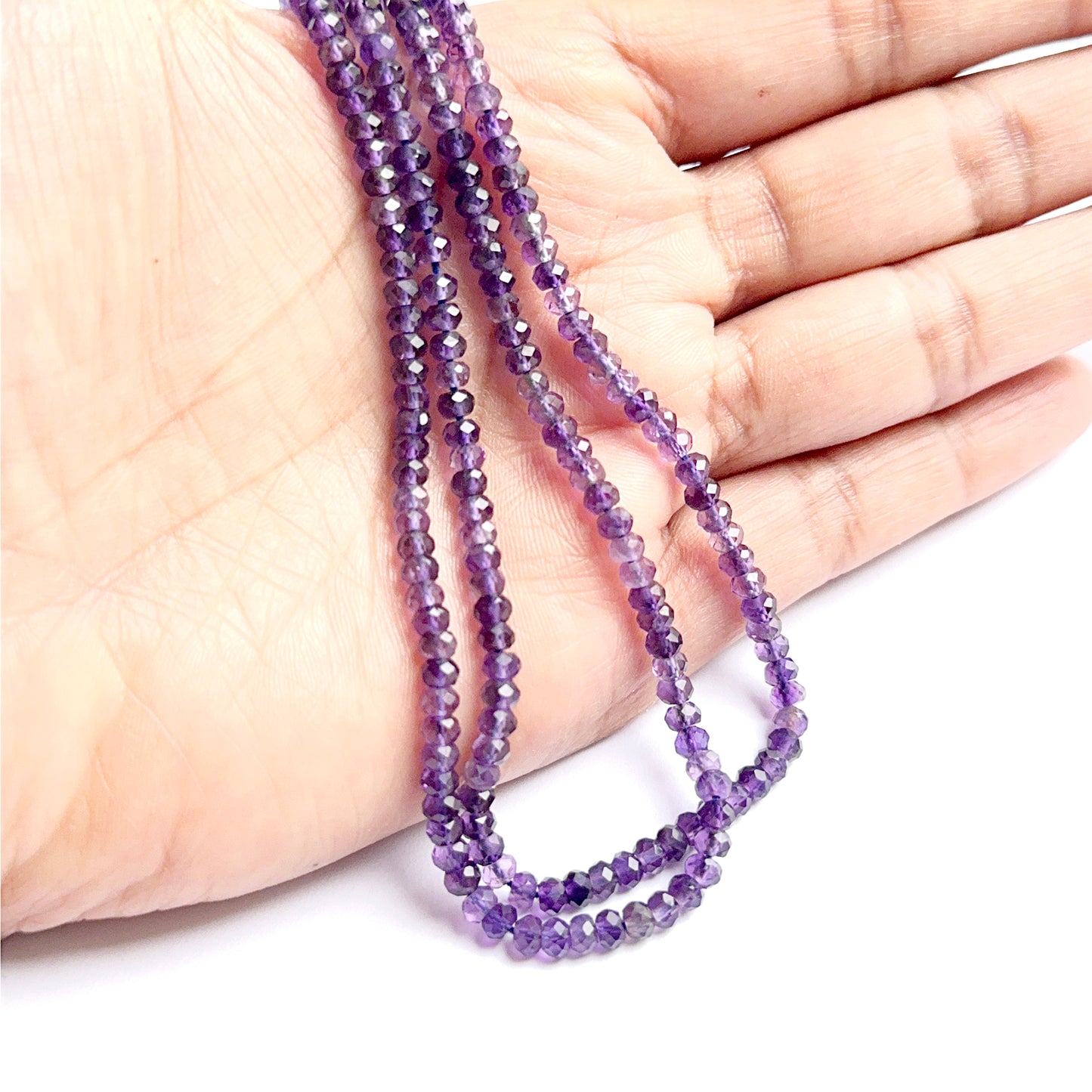 A person holds delicate strands of amethyst beads, showcasing their smooth design.