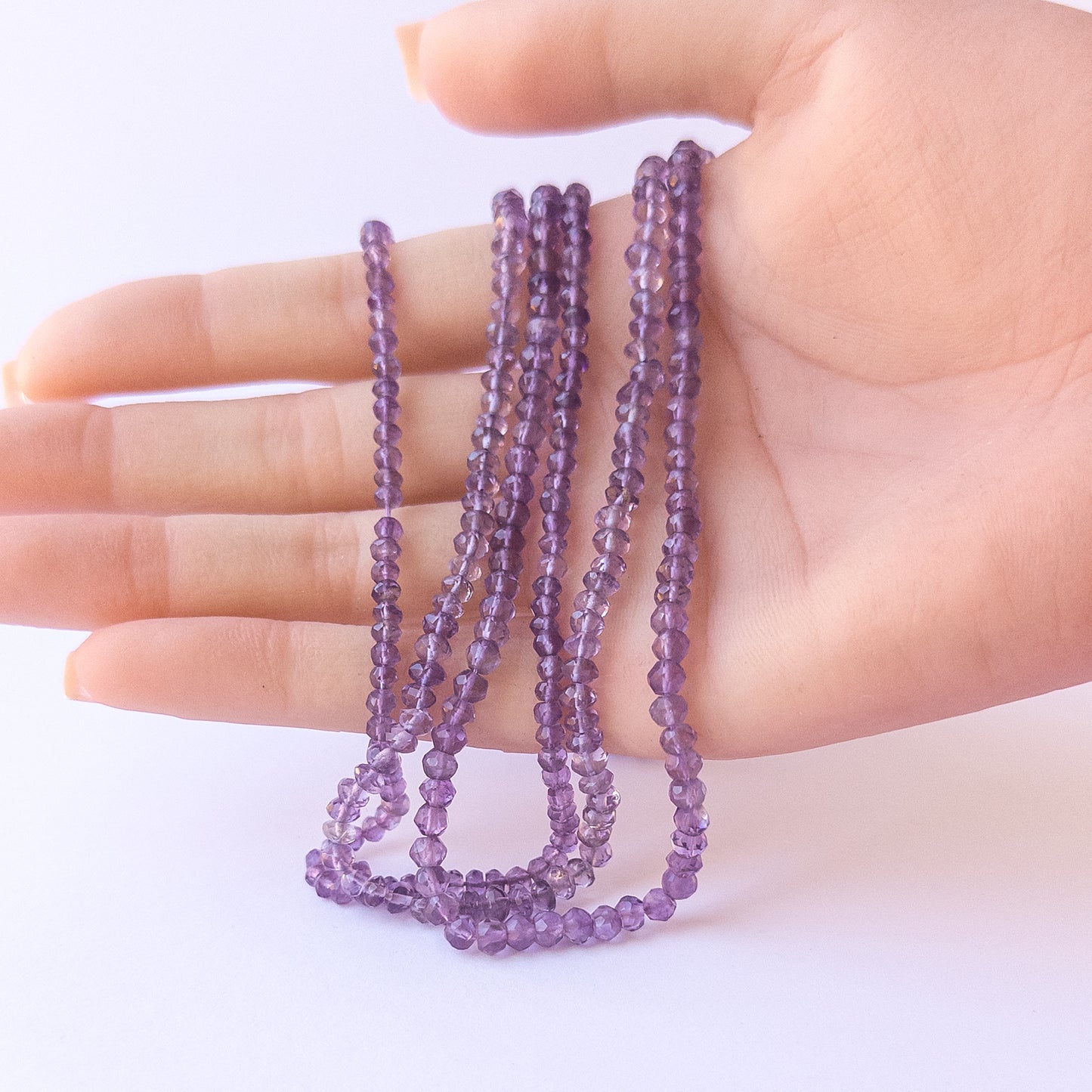 A person holds delicate strands of Amethyst beads, showcasing their faceted rondelle design.