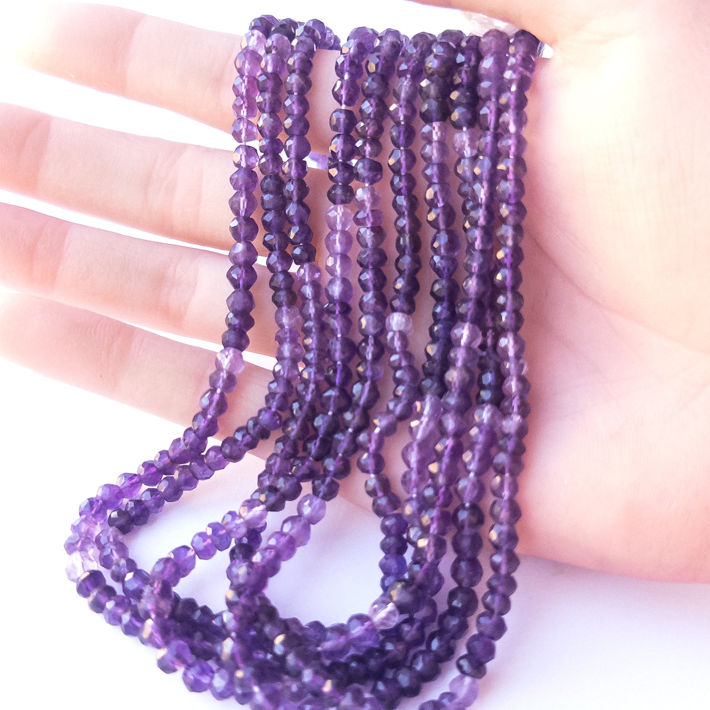 A person holds delicate strands of Amethyst beads, showcasing their faceted rondelle design.