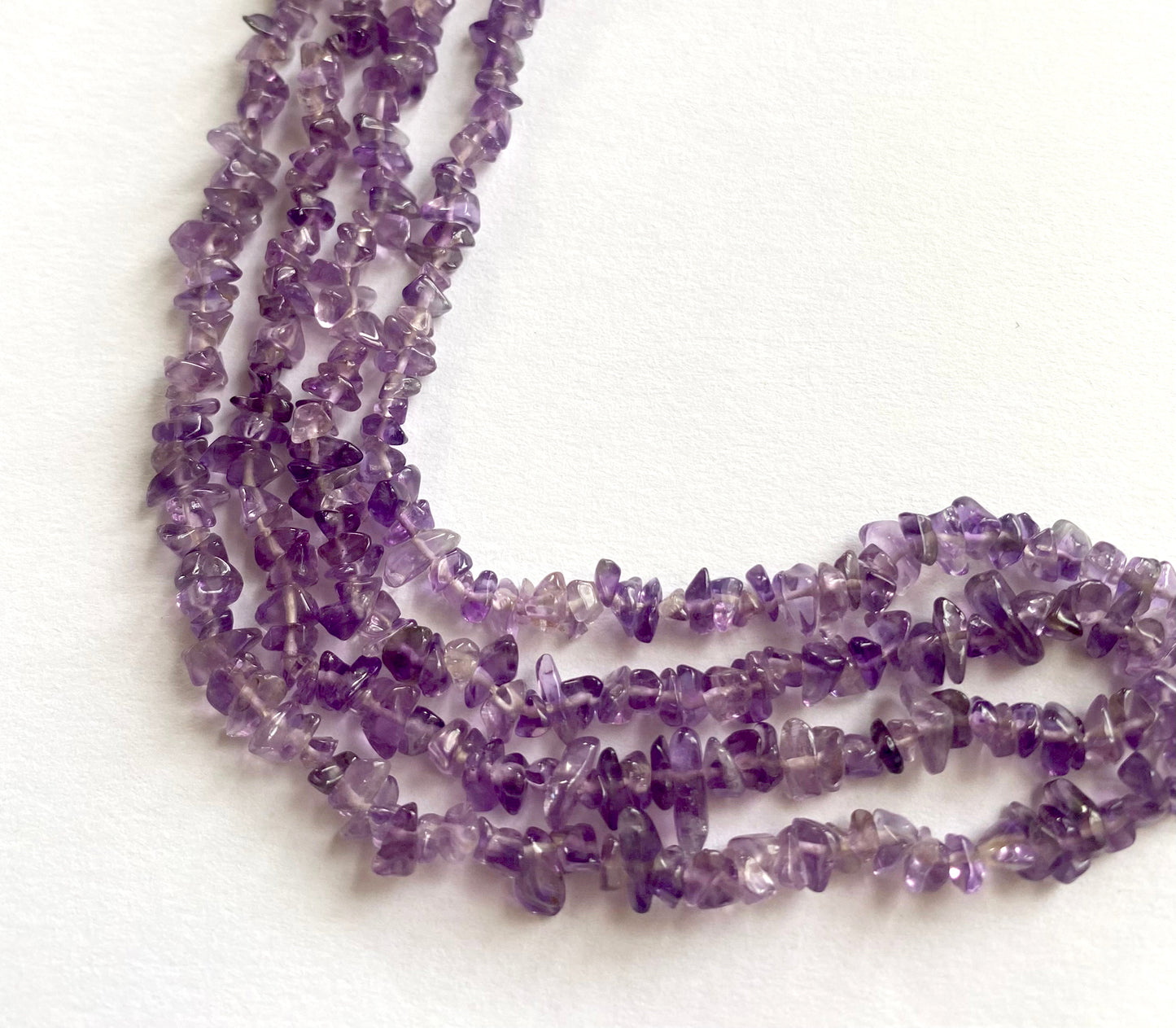 Amethyst smooth chip beads with mixed purple hues laid out in a natural curve on fabric.