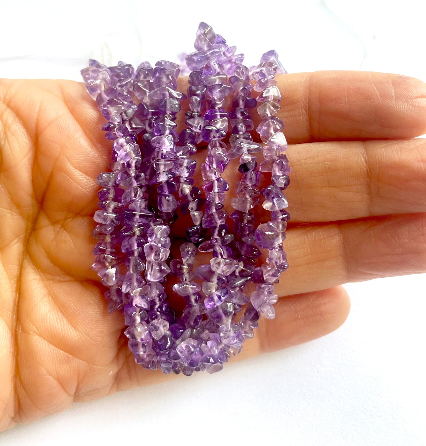 A person holds delicate strands of Amethyst beads, showcasing their smooth design.
