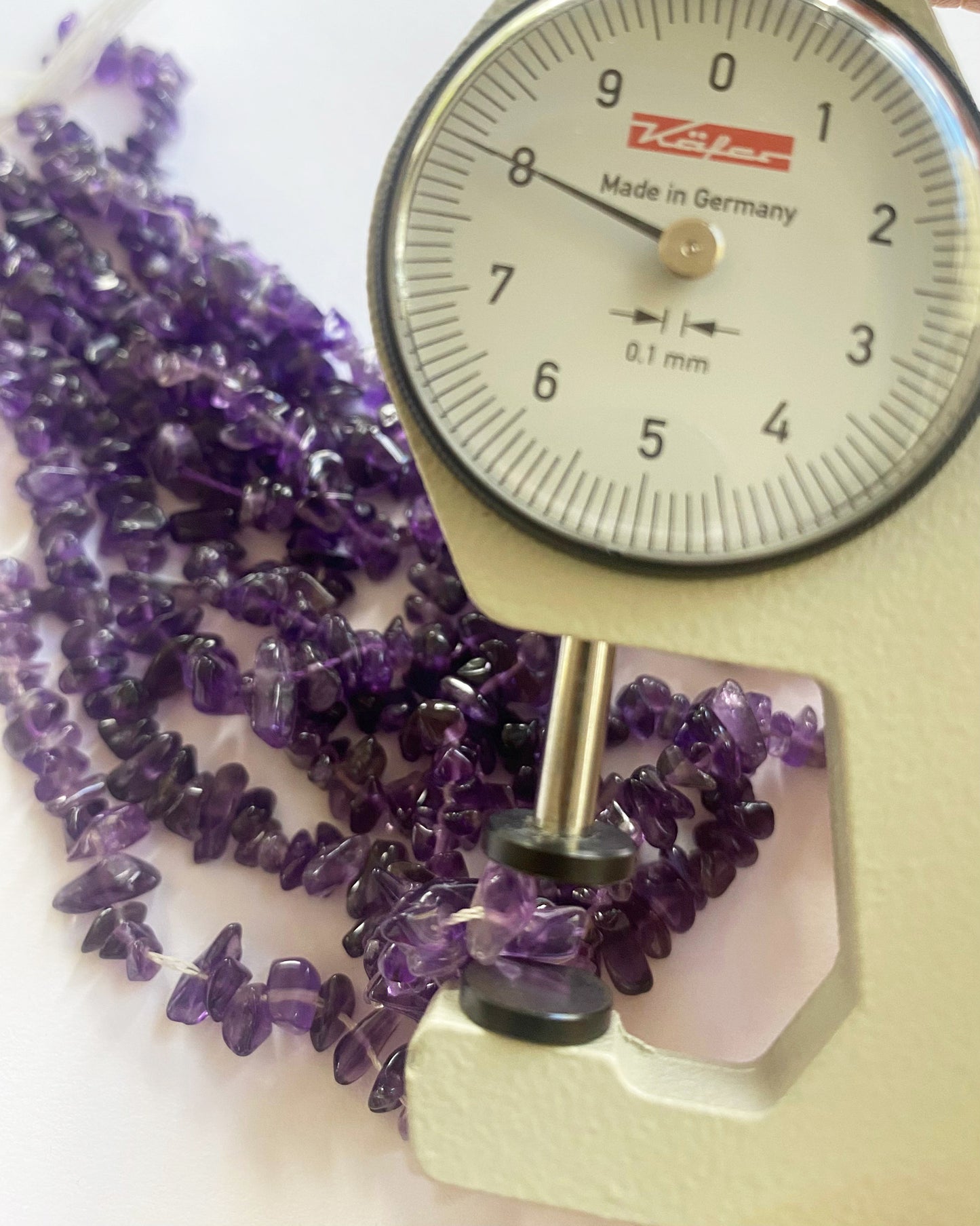 A person holds delicate strands of Amethyst beads, showcasing their smooth design.