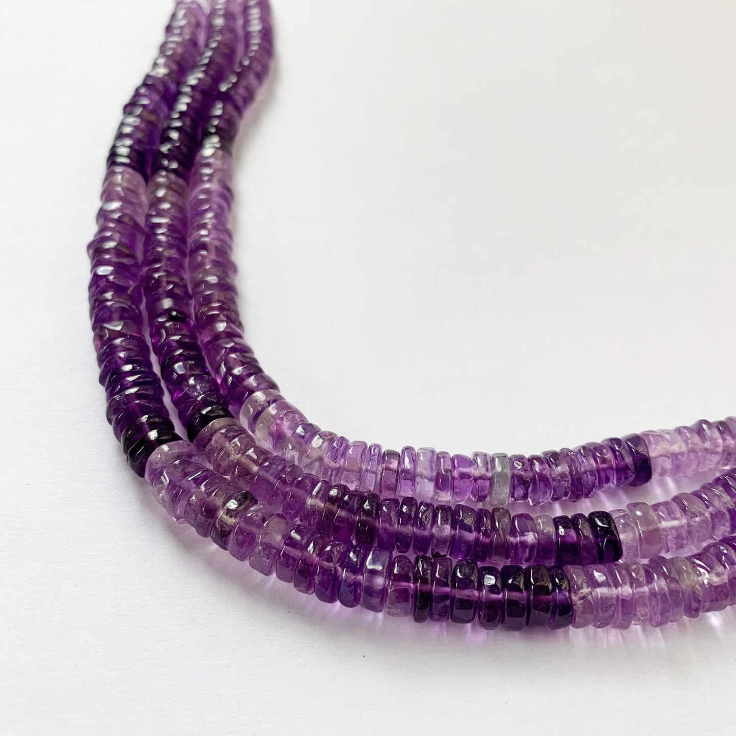 A person holds delicate strands of Amethyst beads, showcasing their smooth design.