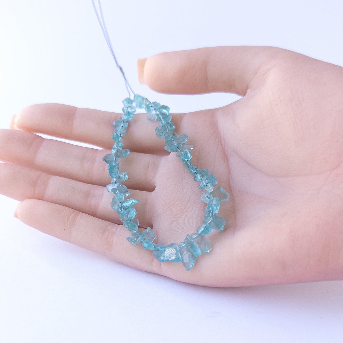 A person holds delicate pieces of Apatite rough beads, showcasing their drilled rough design.